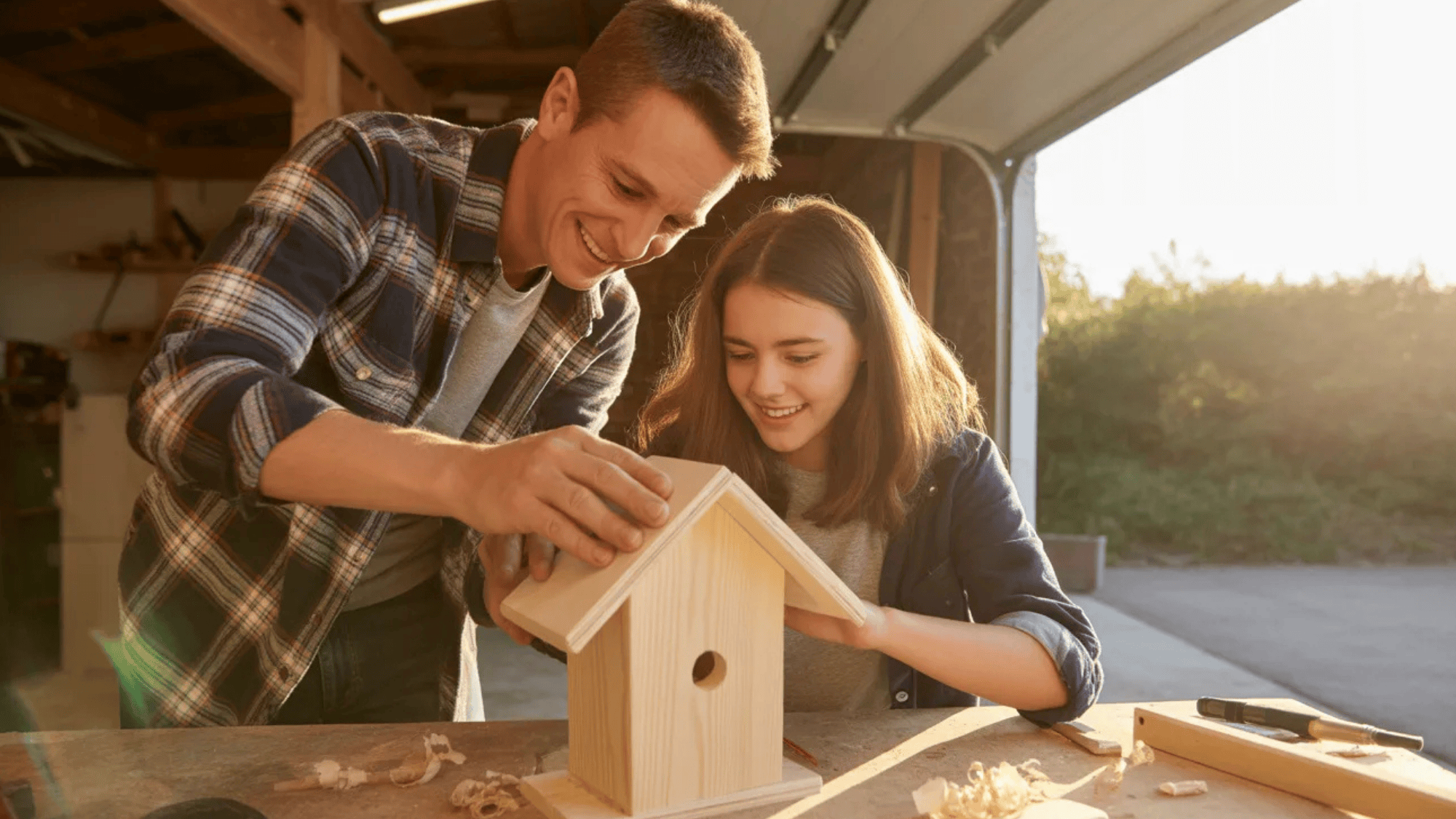 a father and daughter building a birdhouse together in a garage workshop