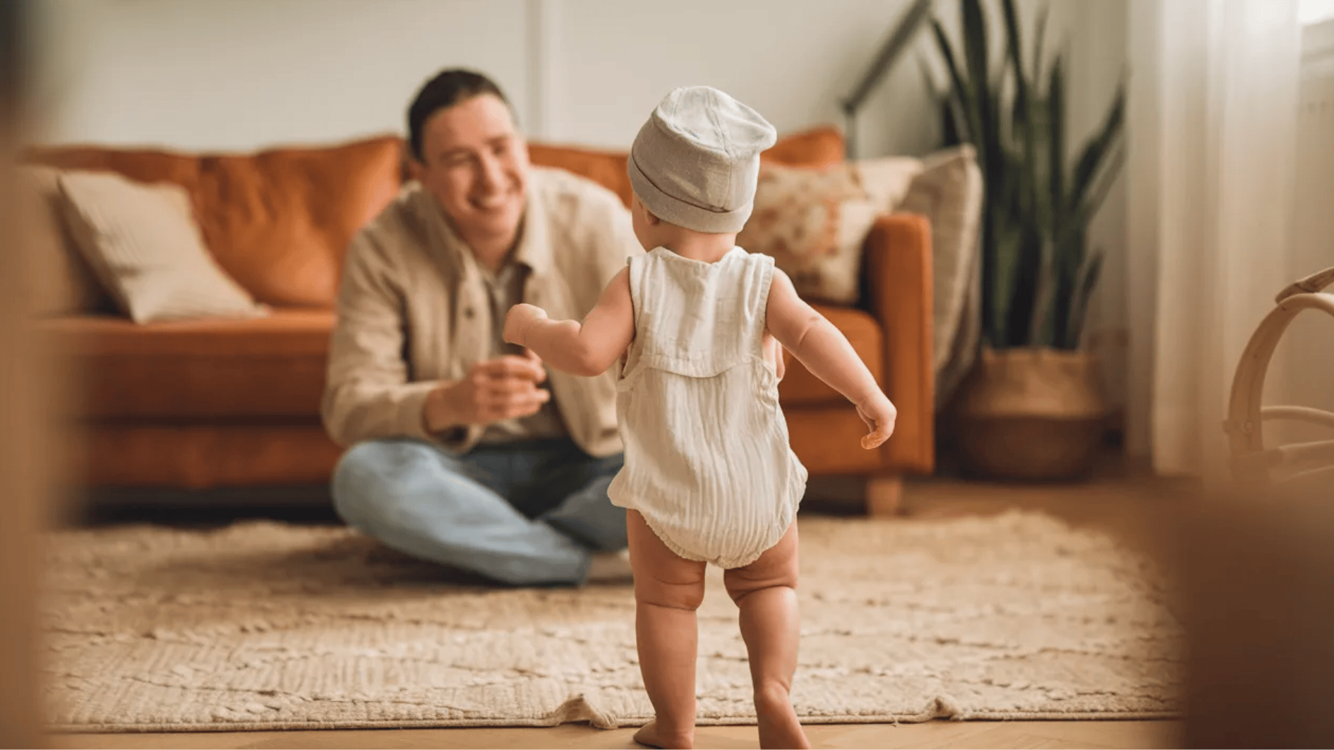 baby taking first steps toward smiling parent sitting on floor in a warm, cozy living room
