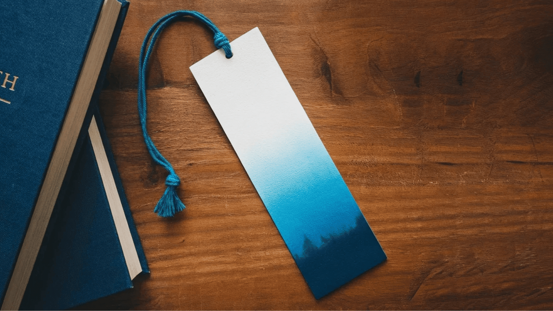 blue hardcover books with a handmade gradient bookmark resting on a wooden surface