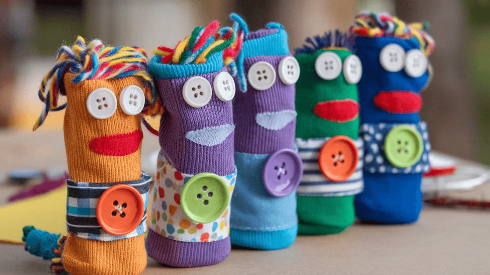 colorful diy sock puppets with button eyes, yarn hair, and fabric decorations arranged on a table for kids craft activity