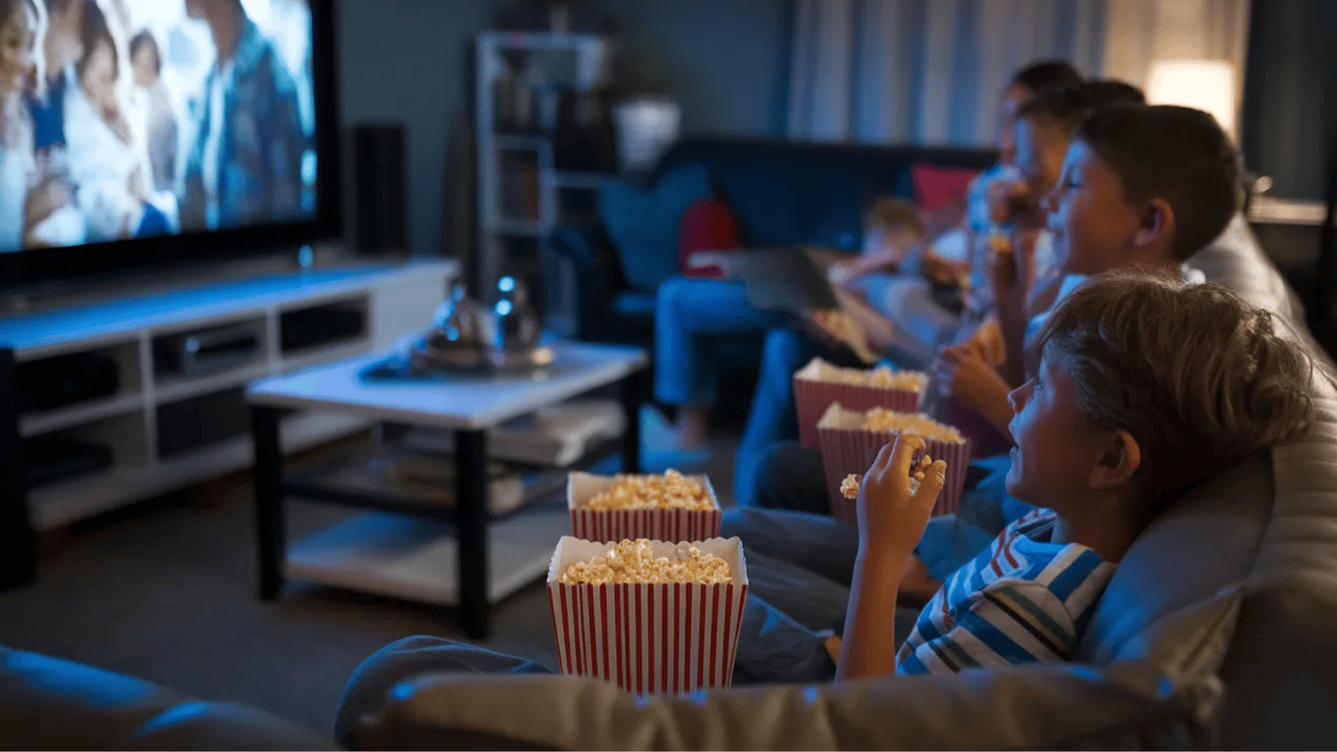 kid along with their siblings having a movie night, eating popcorn and sitting on a cozy couch with dim lights, a family movie playing on the projector screen