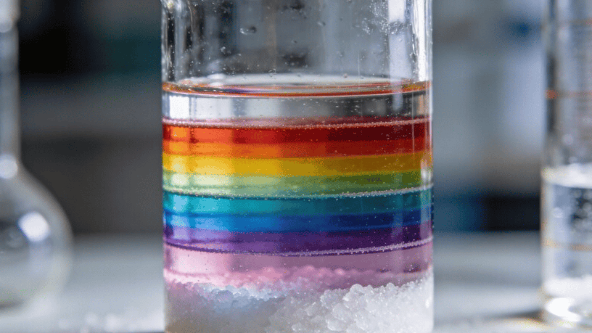 layered colored saltwater density tower in a clear glass, vivid rainbow bands, visible separation lines