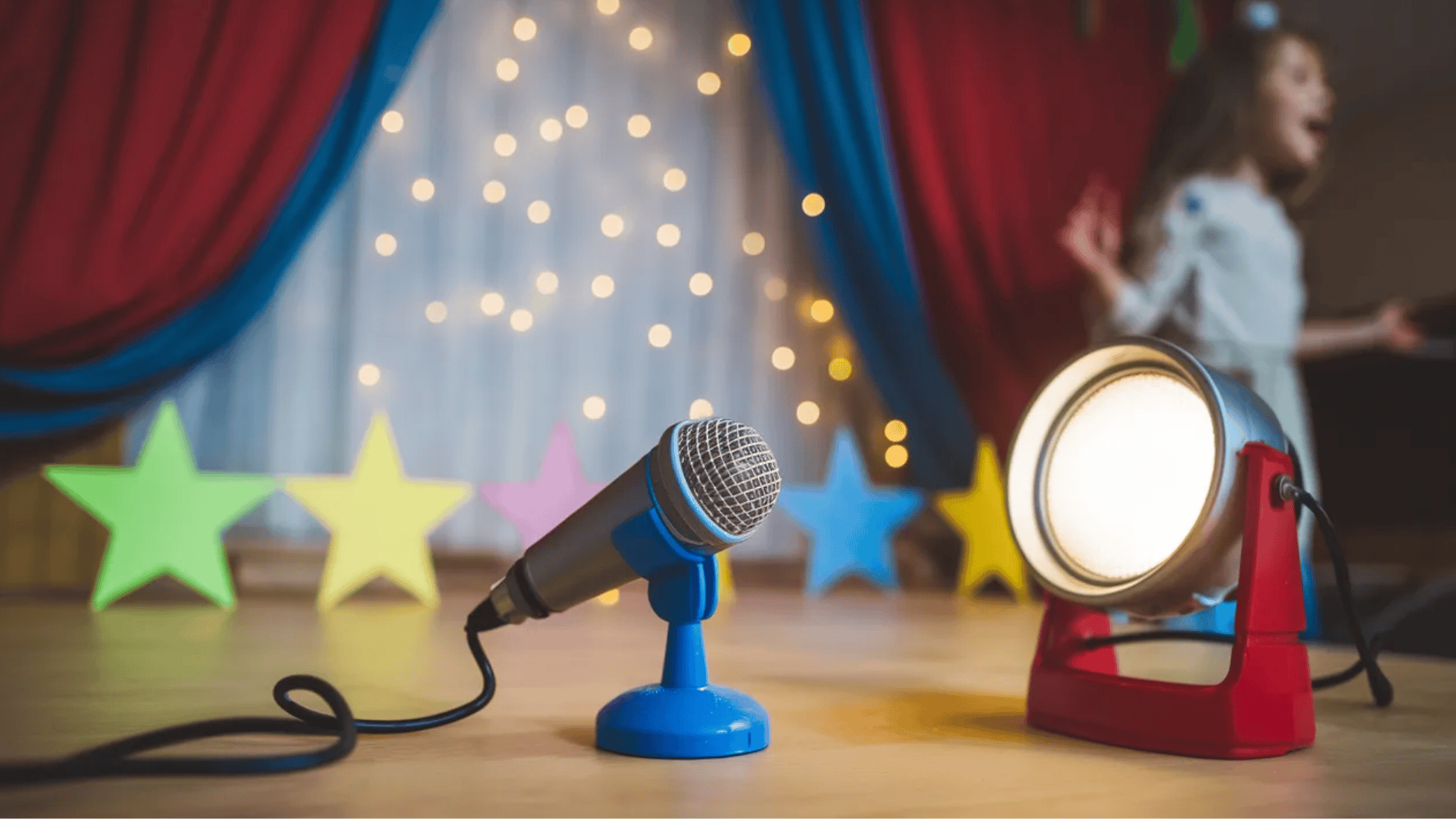 toy microphone and spotlight on small stage with colorful star decorations and child performing in background