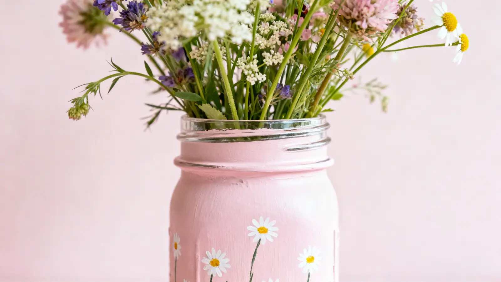 Glass jar painted pink with small white flower designs holding a bouquet of mixed flowers