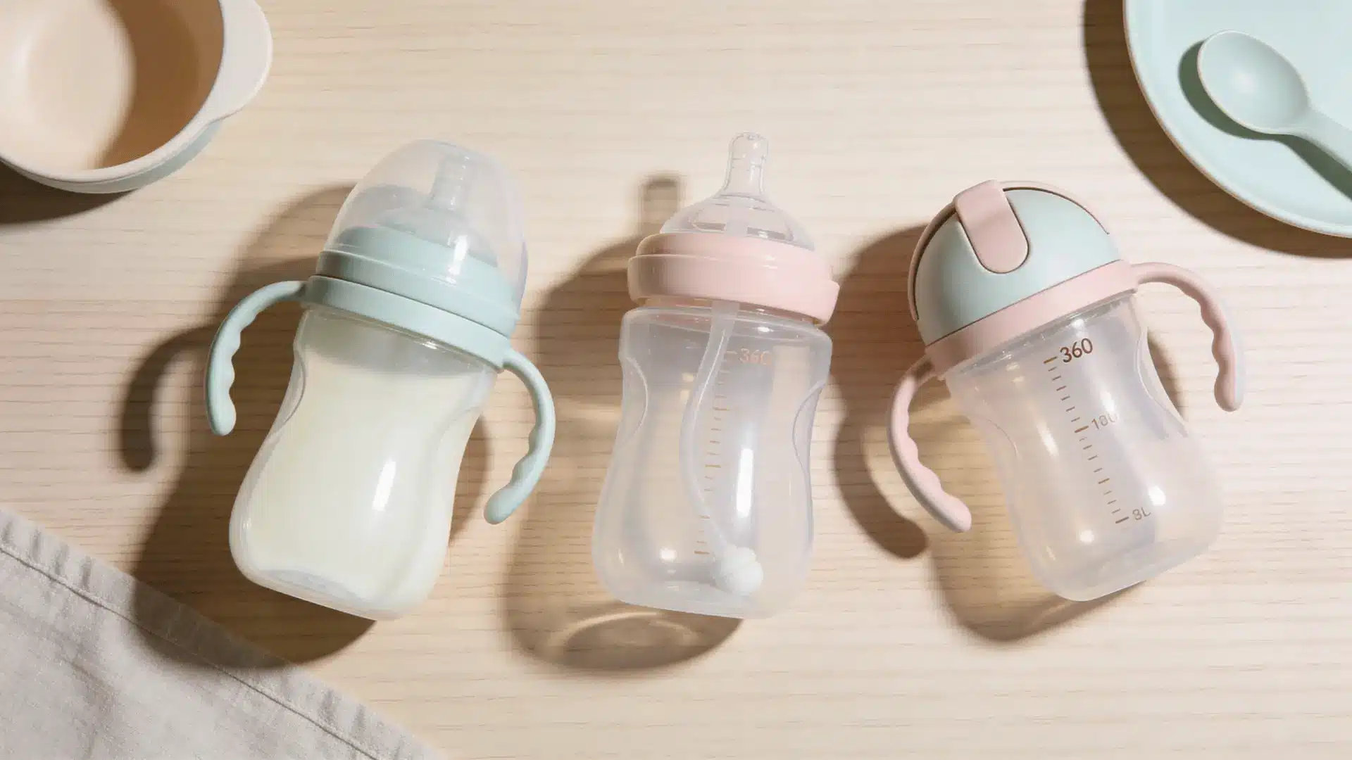 Three types of sippy cups soft spout straw and 360 cup arranged on table with baby bowl and spoon in soft natural light