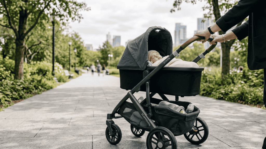 baby sleeping in a black stroller being pushed through a park path with city skyline in the background