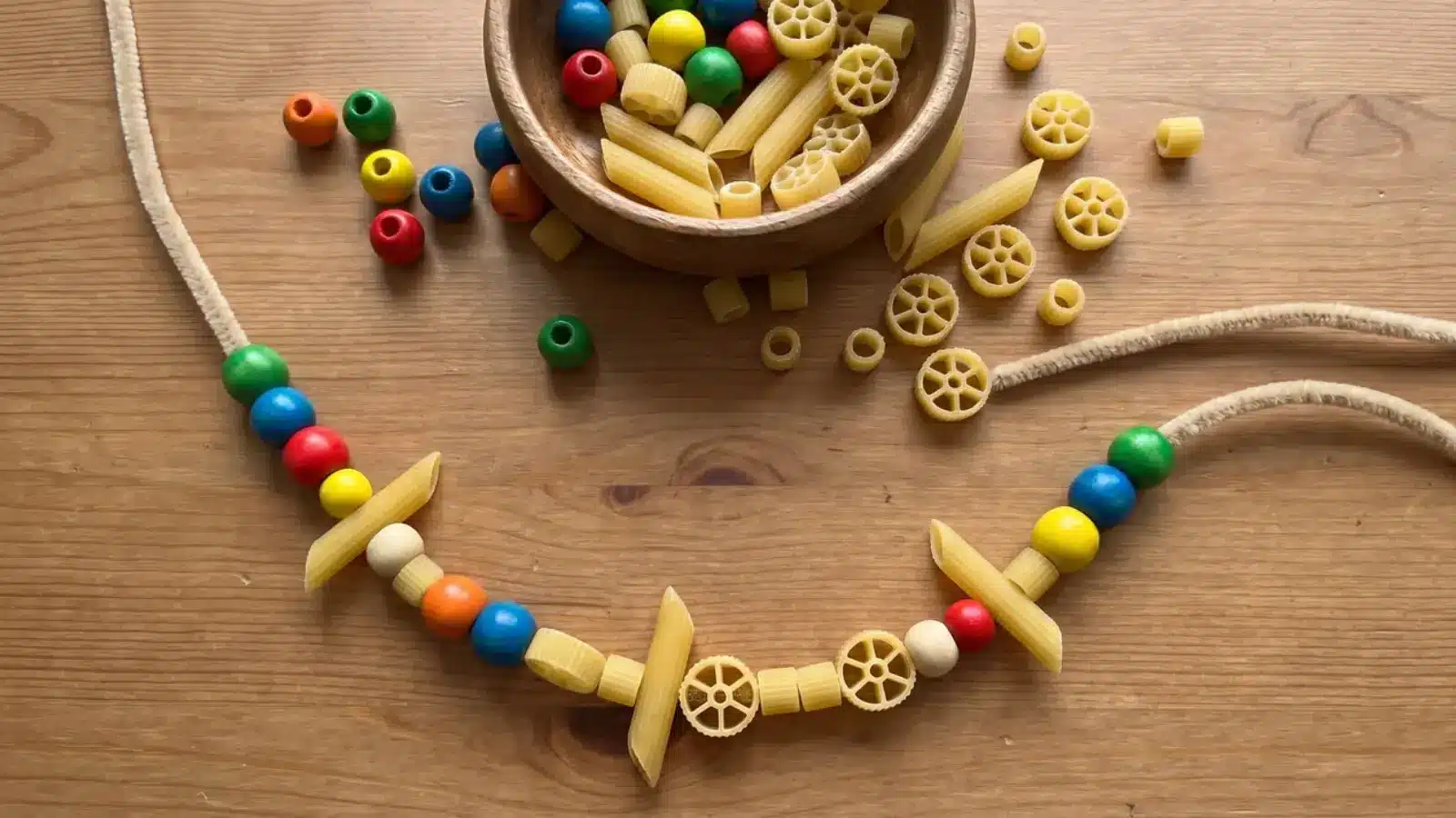 Beads and pasta threaded onto a string with some loose pieces on a table