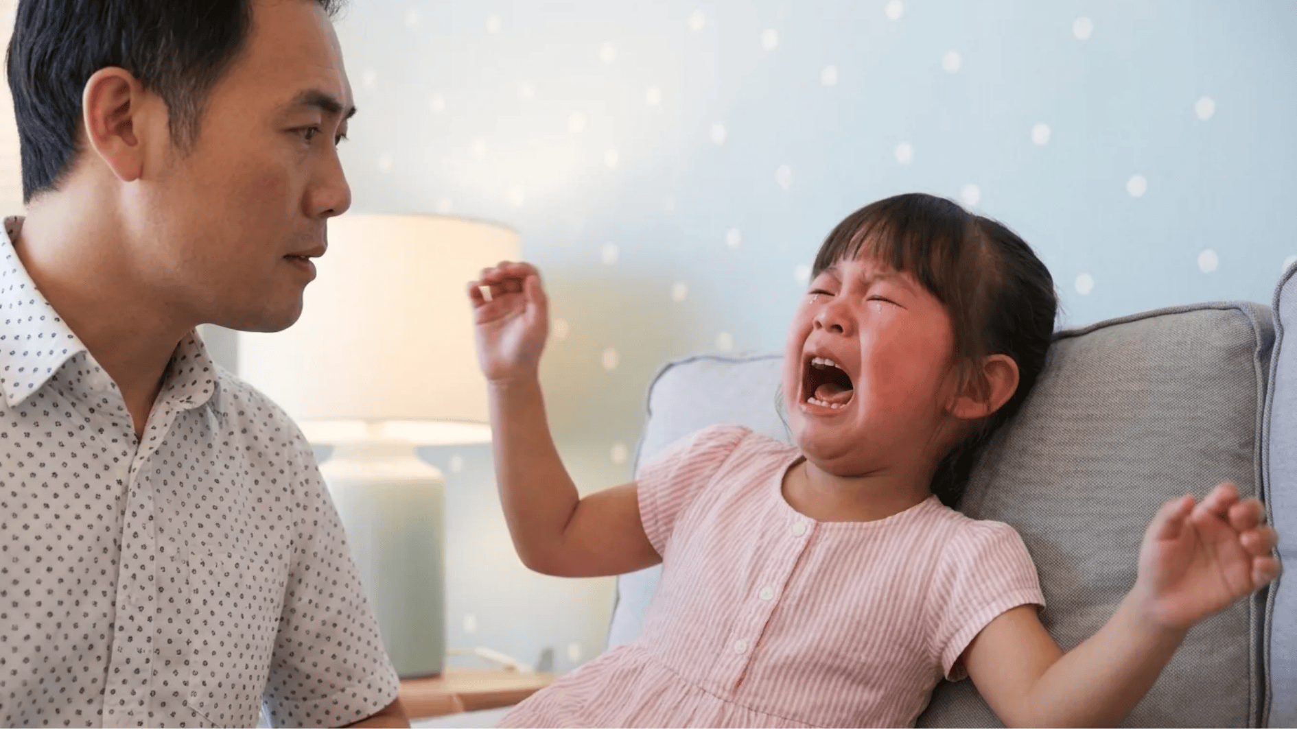 child crying on couch while father looks on with concern in a home setting