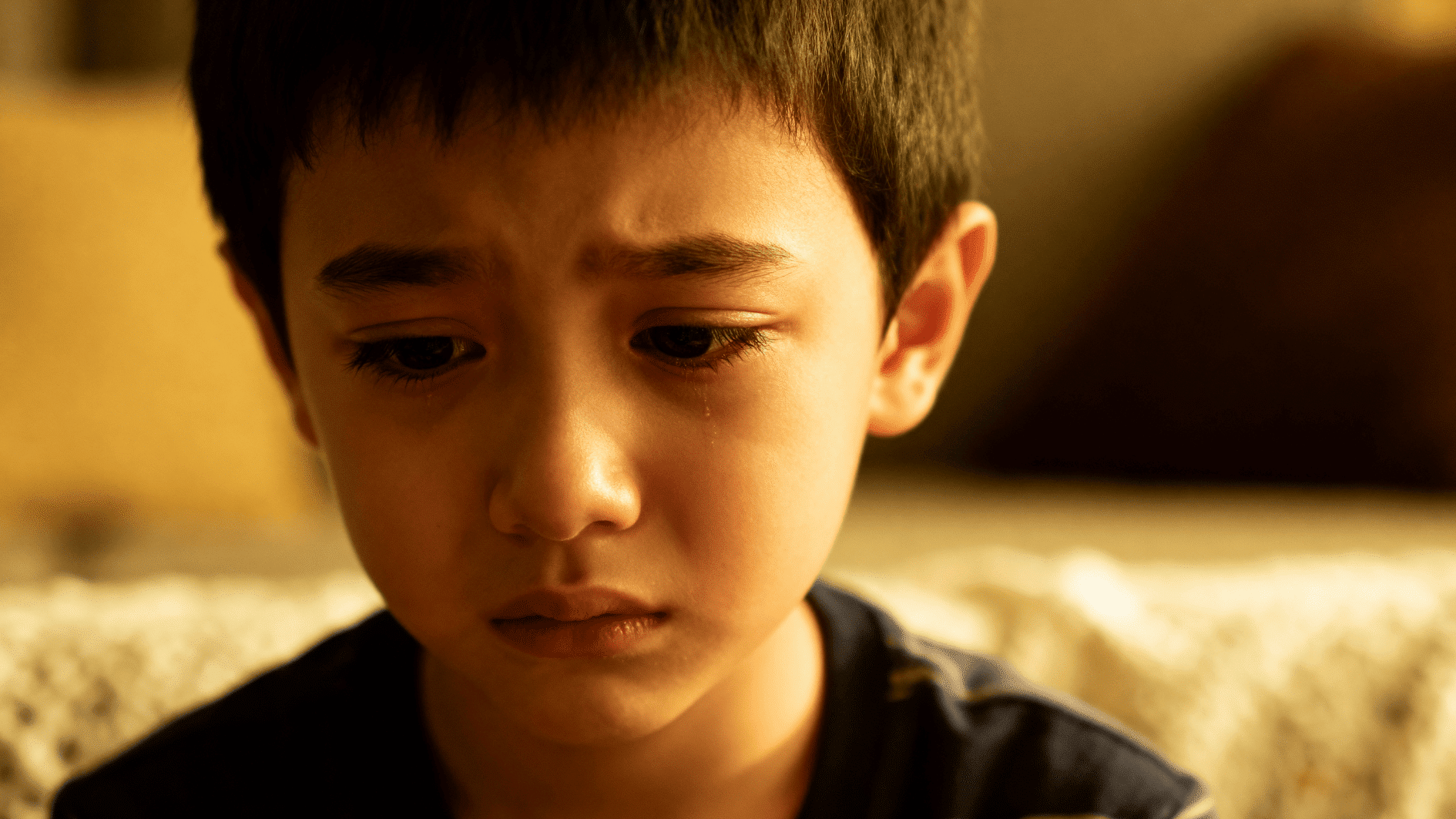 close-up of sad child with tear on cheek, looking down in soft light, conveying loneliness or emotional pain