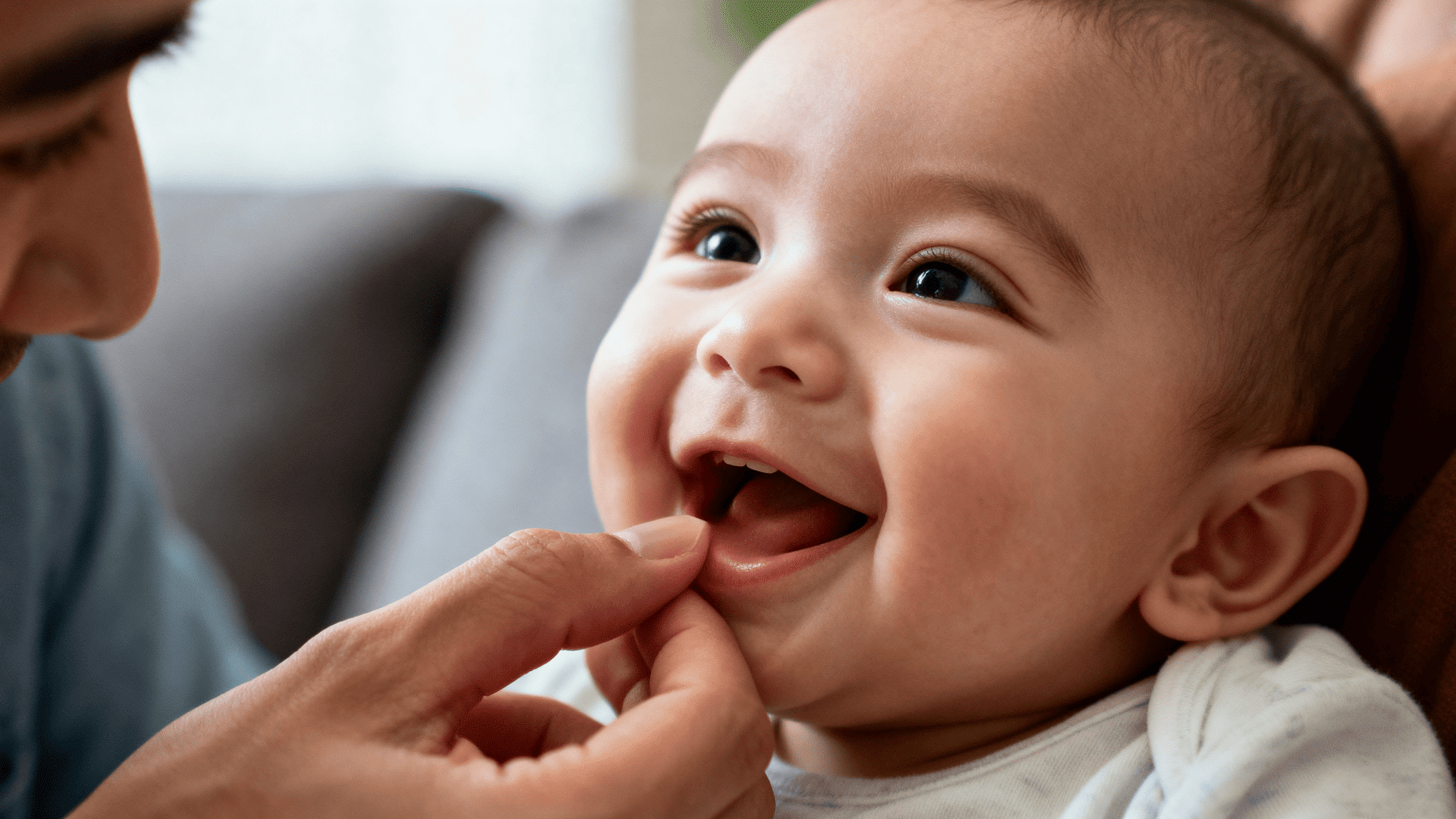 close-up of smiling baby as adult gently checks emerging tooth, showing care, bonding, and early dental development