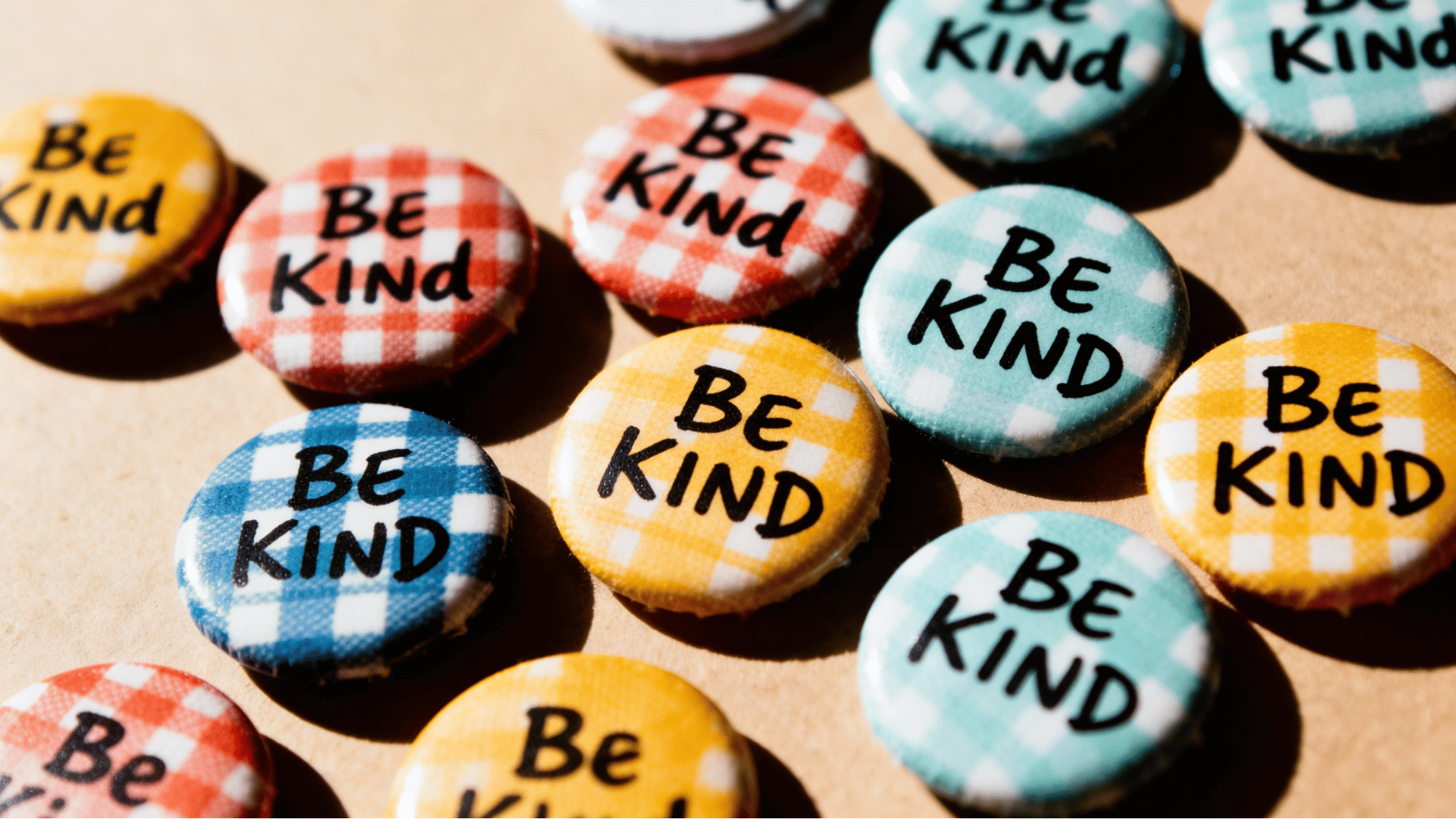 colorful “be kind” badges with checkered patterns arranged closely together on a flat surface
