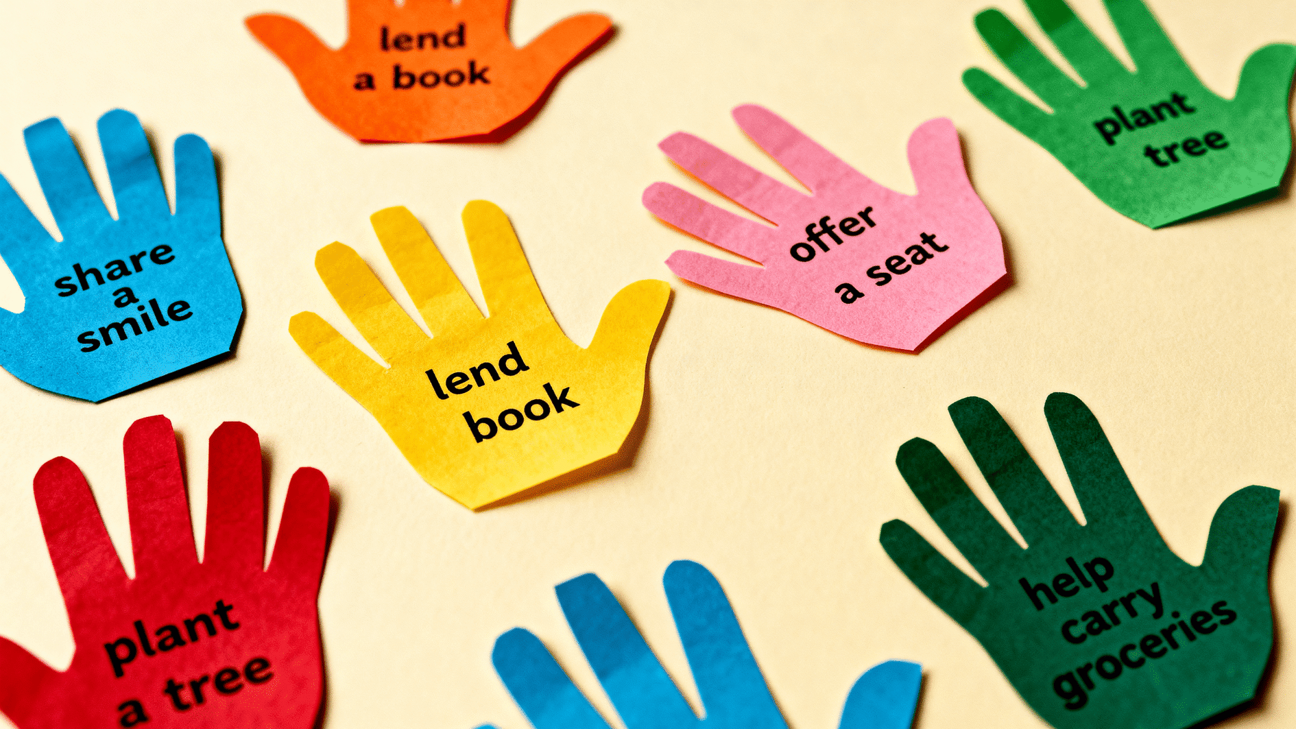 colorful paper hand cutouts with kindness acts like “lend a book” and “help carry groceries” displayed on table