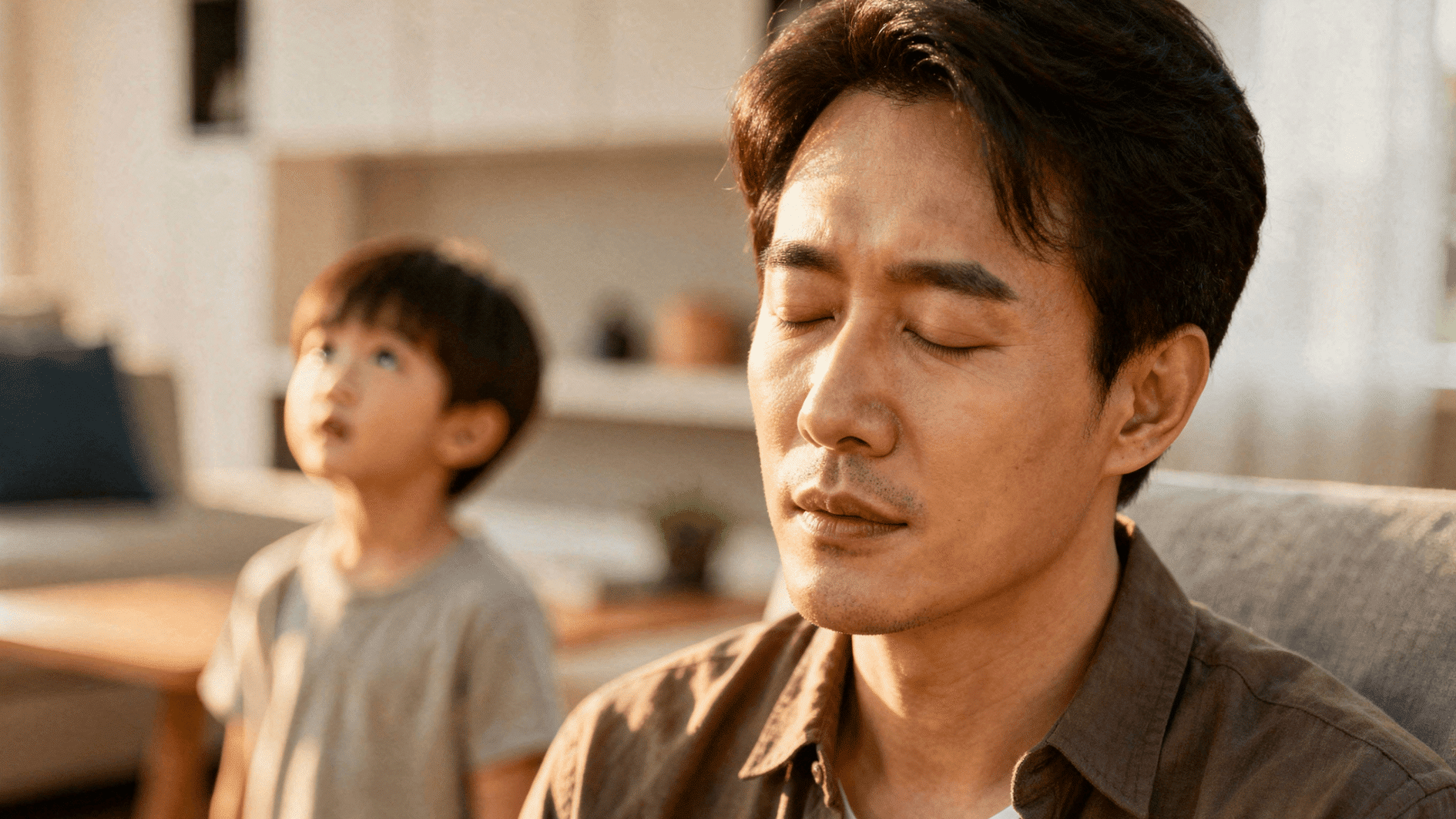 father sits with eyes closed while child looks on, suggesting tension, stress, or emotional distance at home