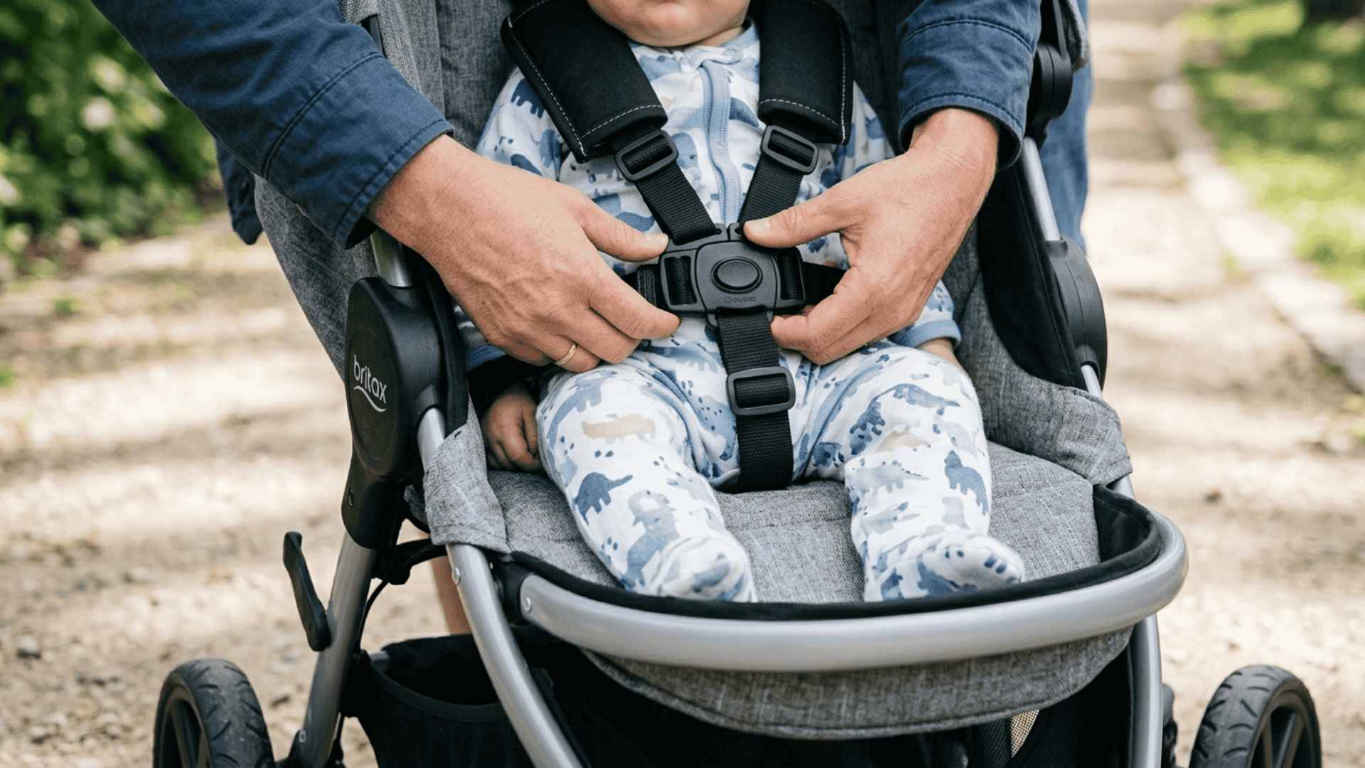 front angle baby stroller with hands fastening safety harness showing secure straps and seat with soft lighting and blurred background