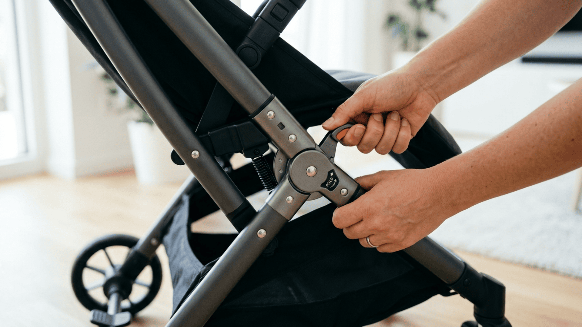hands folding baby stroller showing simple mechanism and strong frame structure with clean background and realistic lighting
