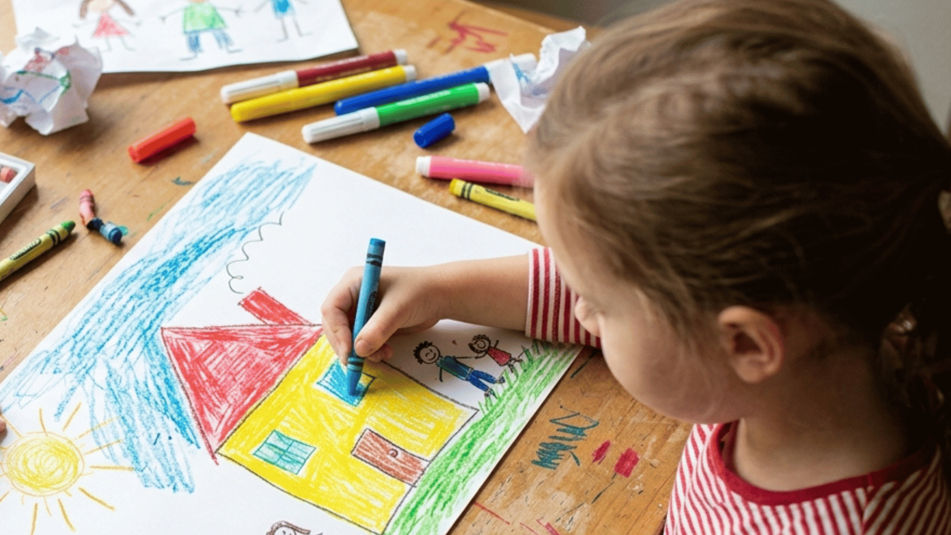kid drawing a colorful house with crayons on paper.