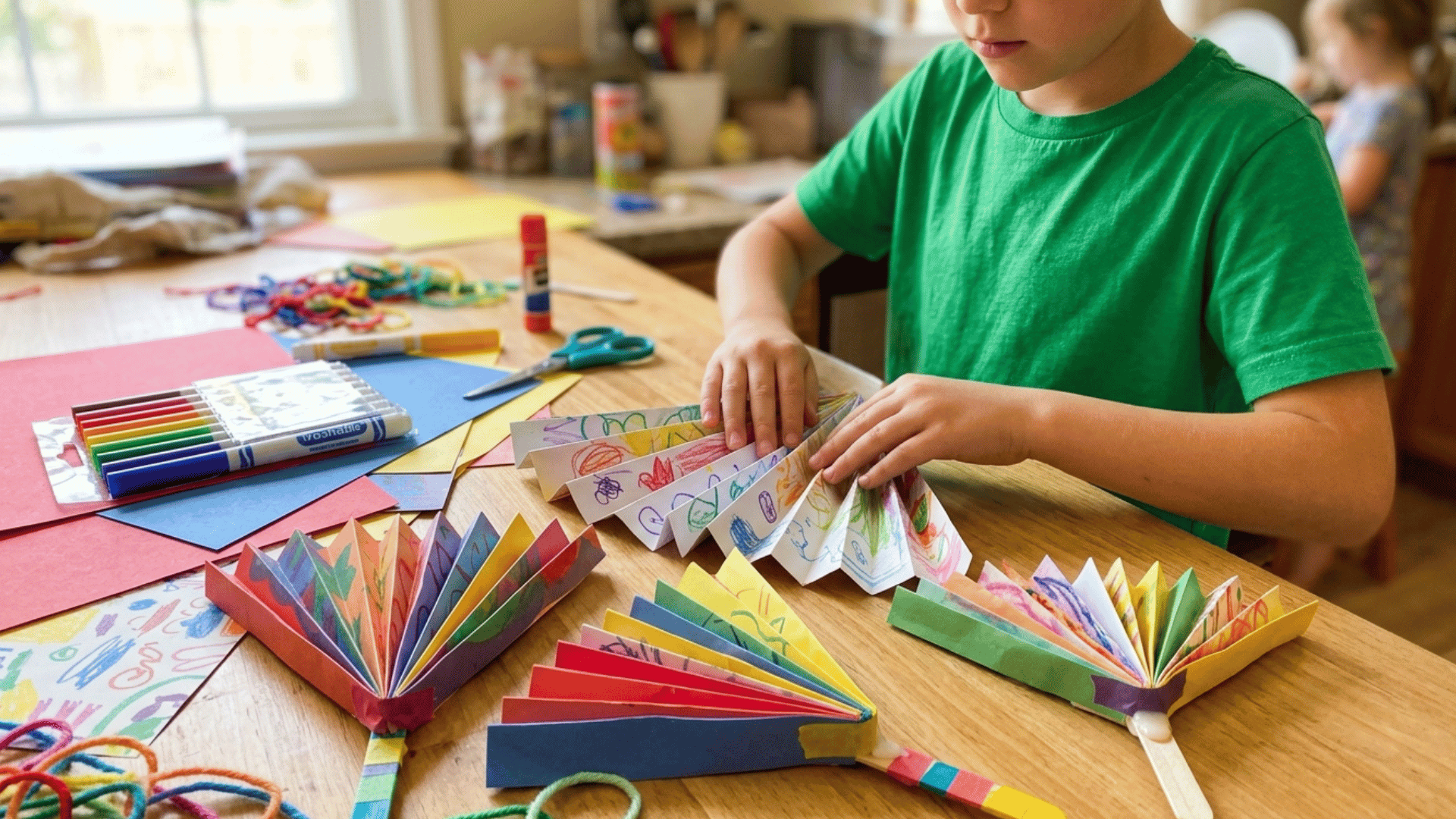kid making folded paper fans with colorful designs at craft table.