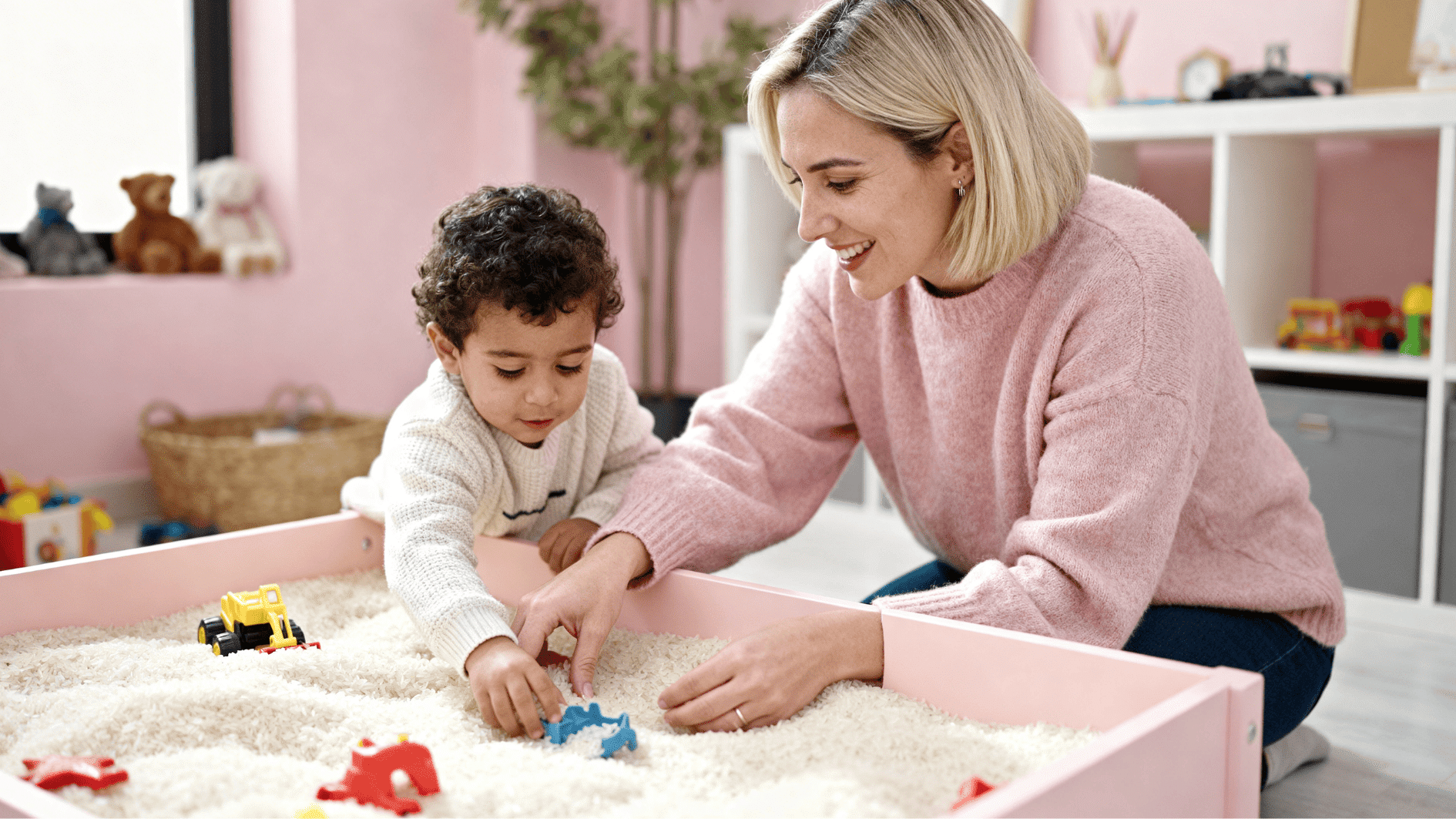 mother and toddler playing with sensory rice bin, exploring textures with toys in a bright, child-friendly playroom setting