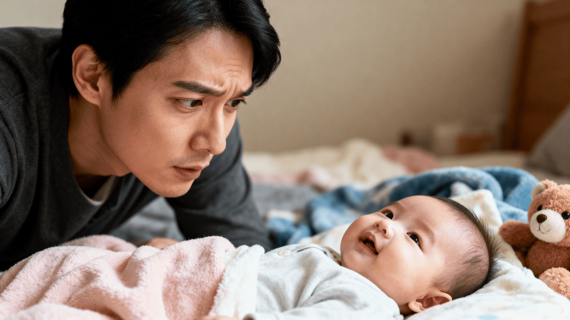 parent leans close to baby lying on bed, sharing attentive eye contact and warm bonding moment at home