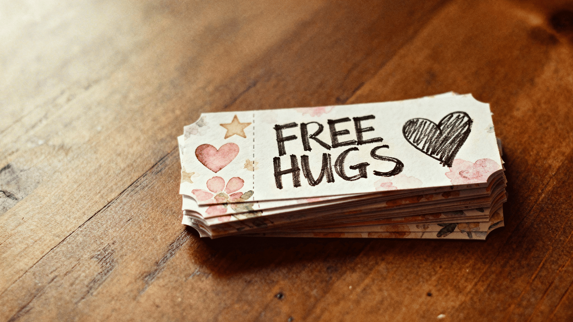 stack of small cards labeled “free hugs” with heart drawings placed on a wooden surface