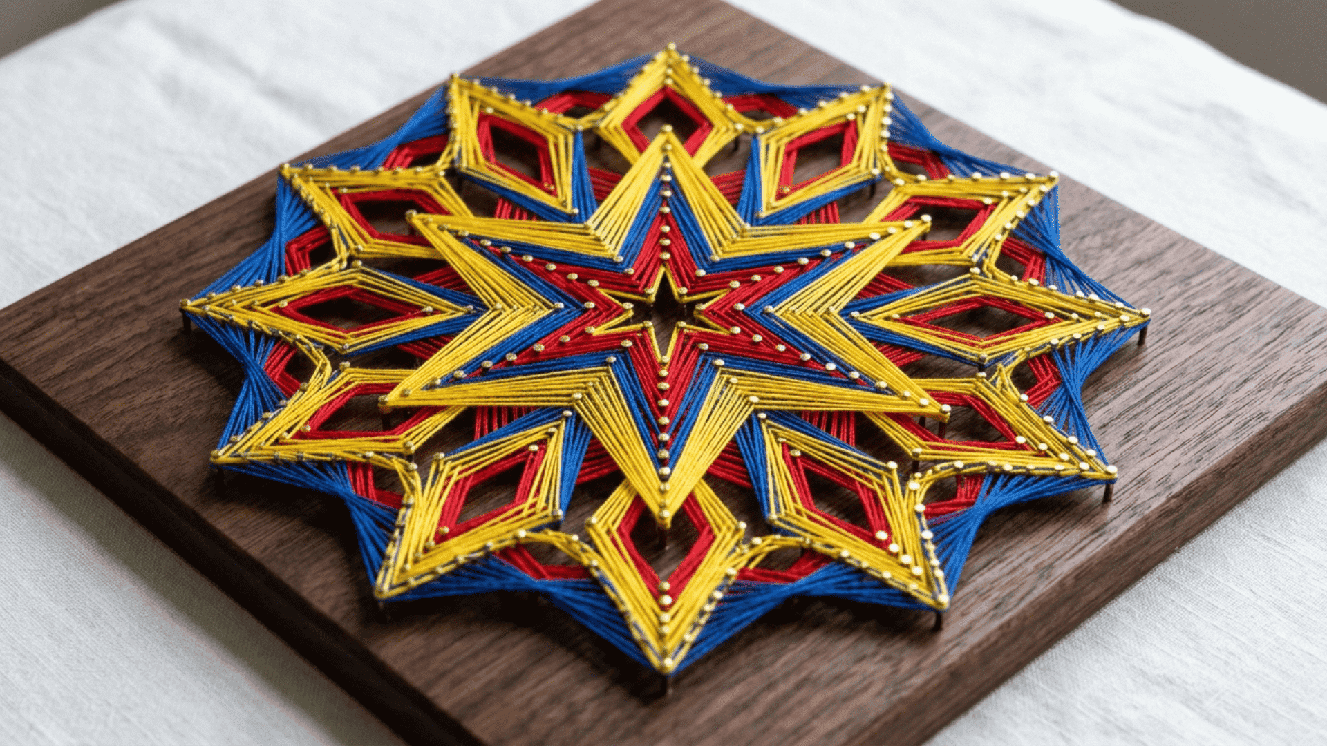string art geometry board with bold star and diamond pattern in red yellow and blue thread on dark wooden board