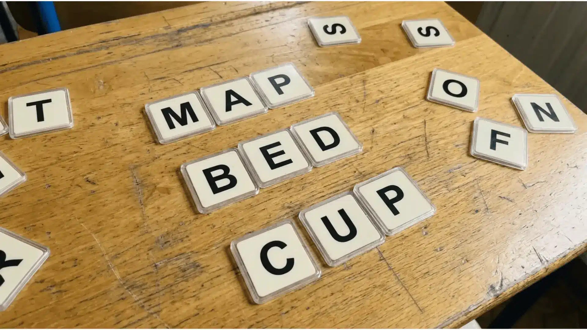 Letter tiles arranged to form CVC words map, bed, and cup on a classroom desk.