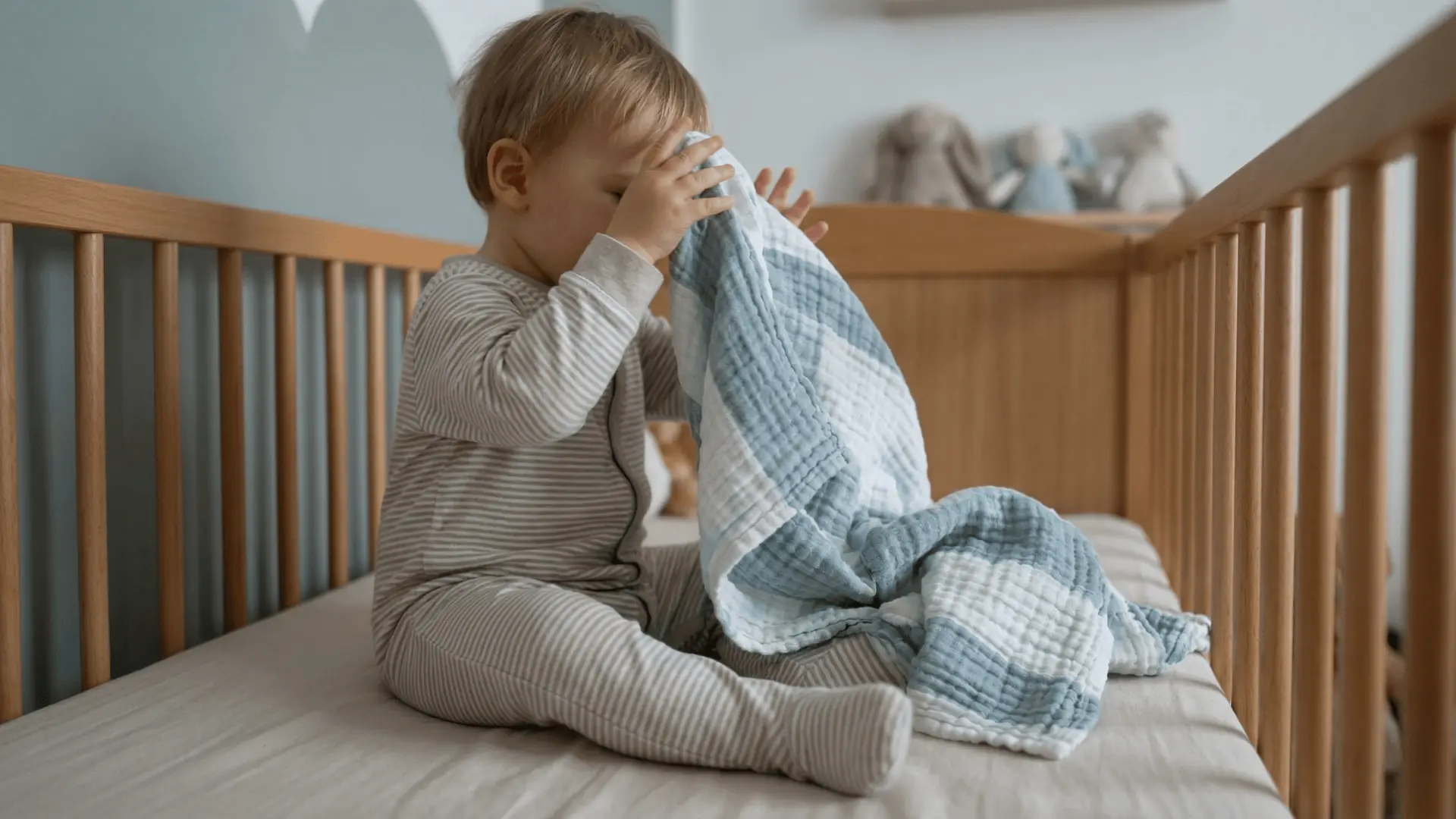 Toddler in crib pushing a blanket away from face