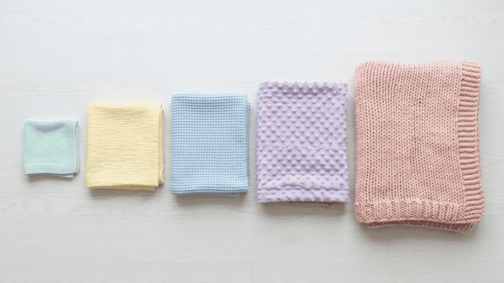 baby blanket size comparison of five different blankets arranged by size on a white surface