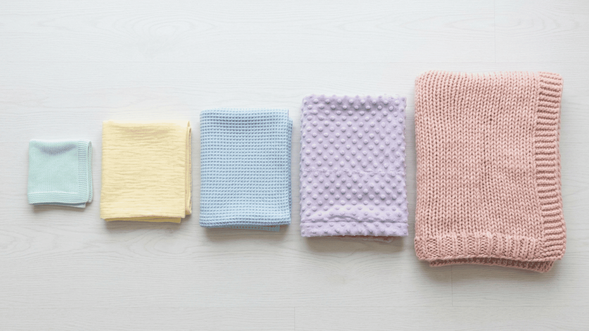 baby blanket size comparison of five different blankets arranged by size on a white surface