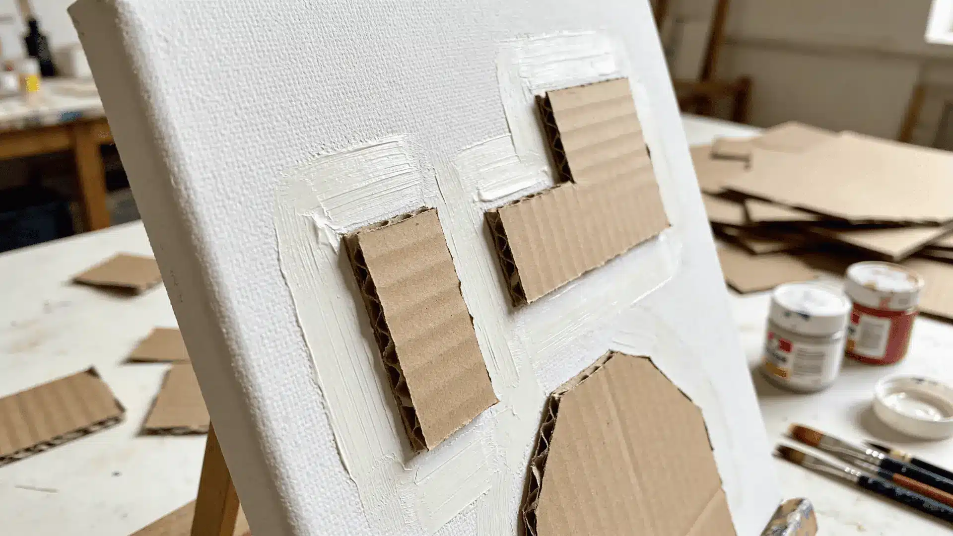 Canvas with raised cardboard shapes painted over showing surface depth on a workspace