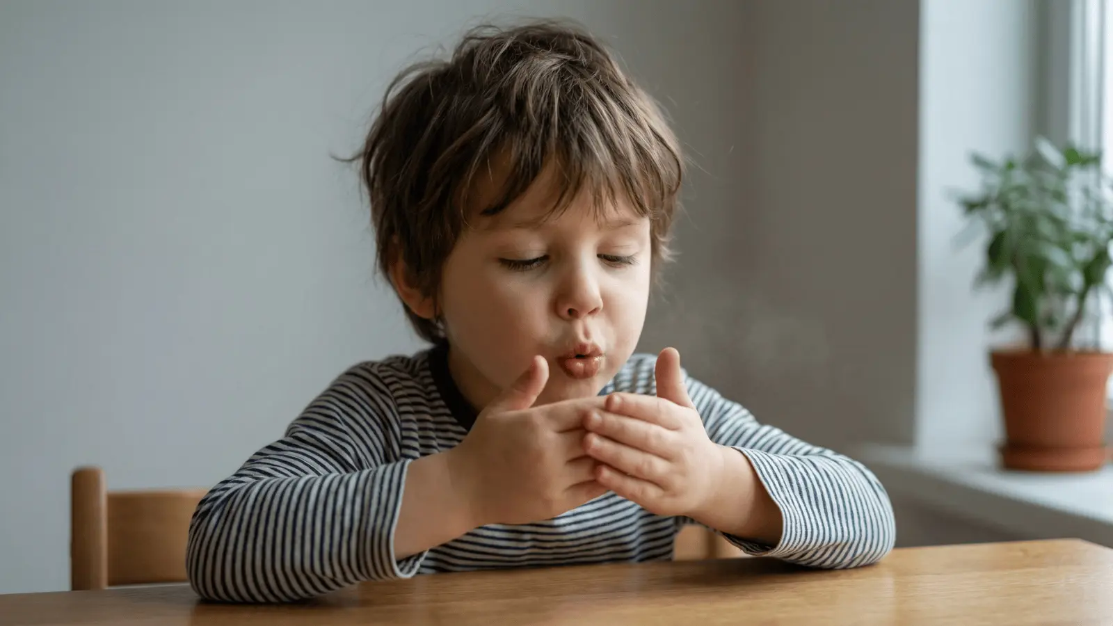 Child slowly blowing air forward as if blowing out candles while sitting at a table