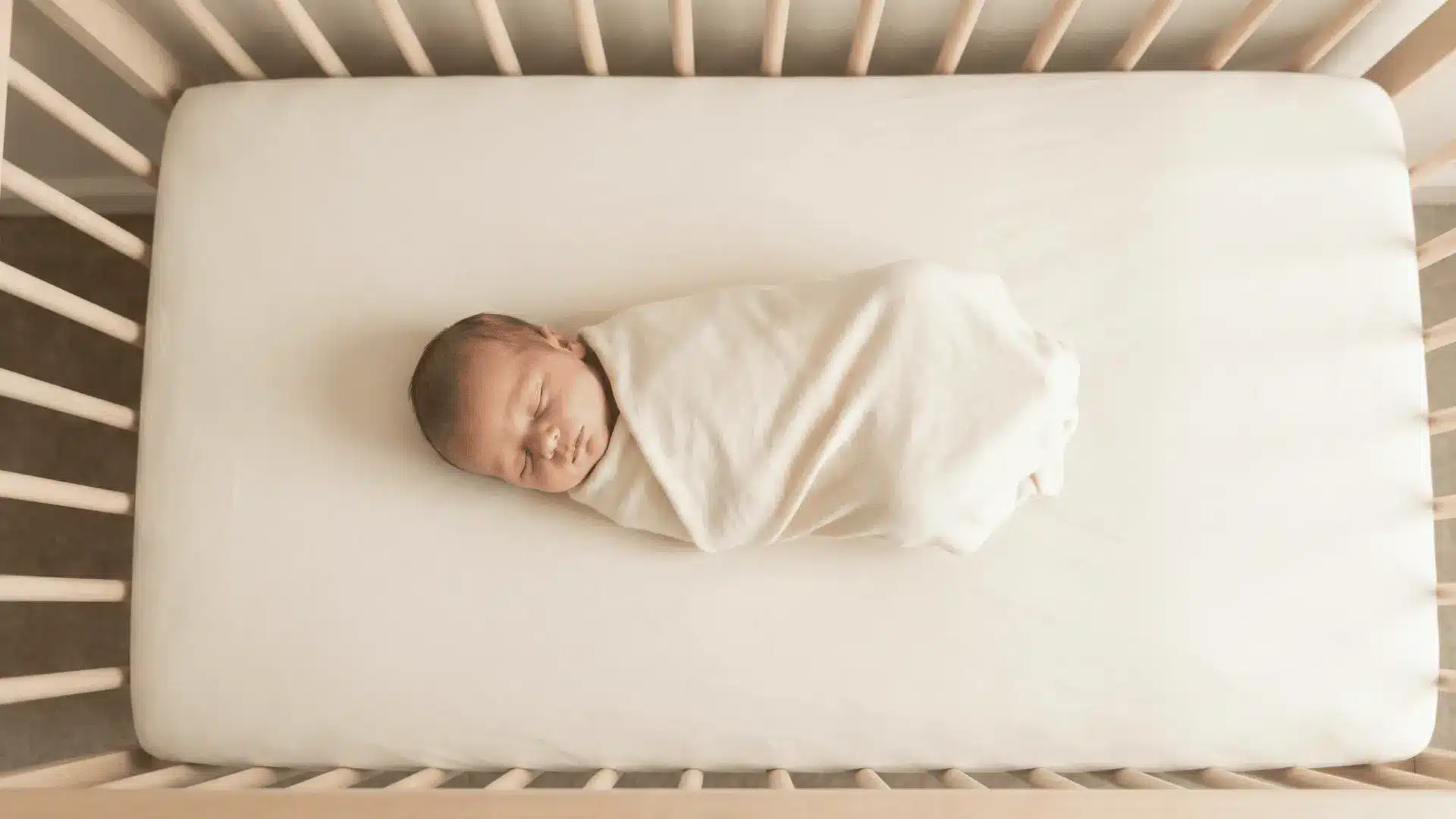 Newborn lying on back in crib with clear sleeping space
