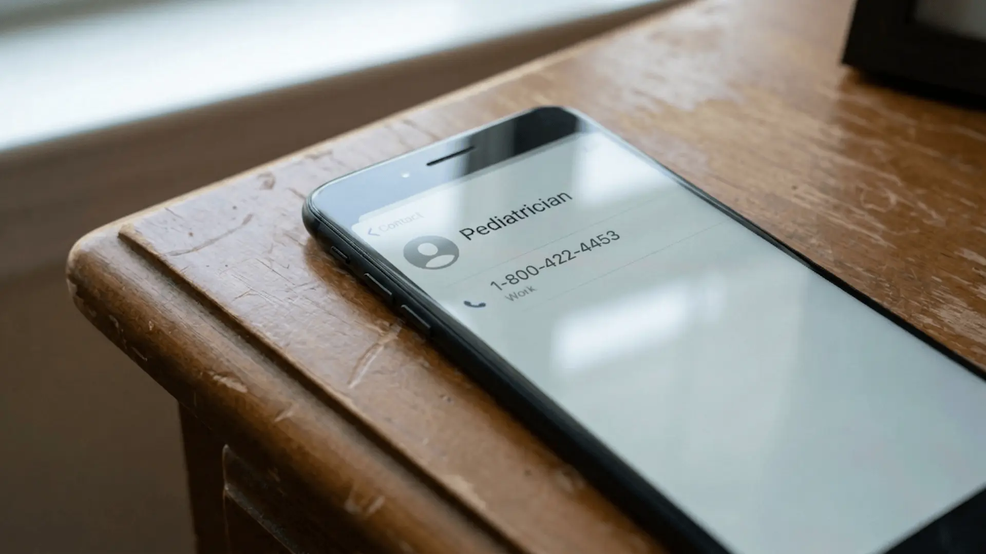 Smartphone screen showing a saved contact named pediatrician on a table.