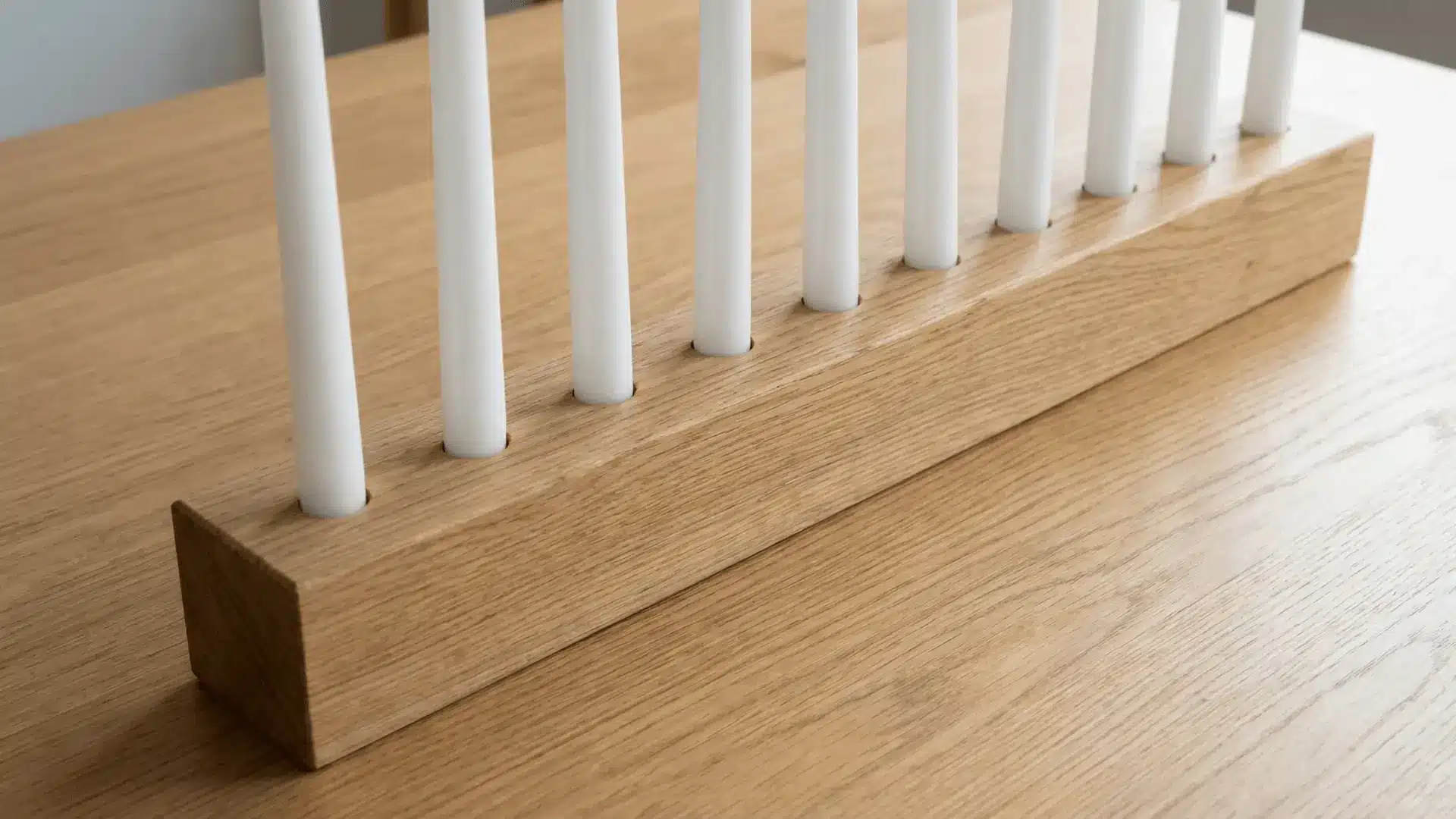 Wooden candle holder with evenly drilled holes holding candles upright on a flat surface