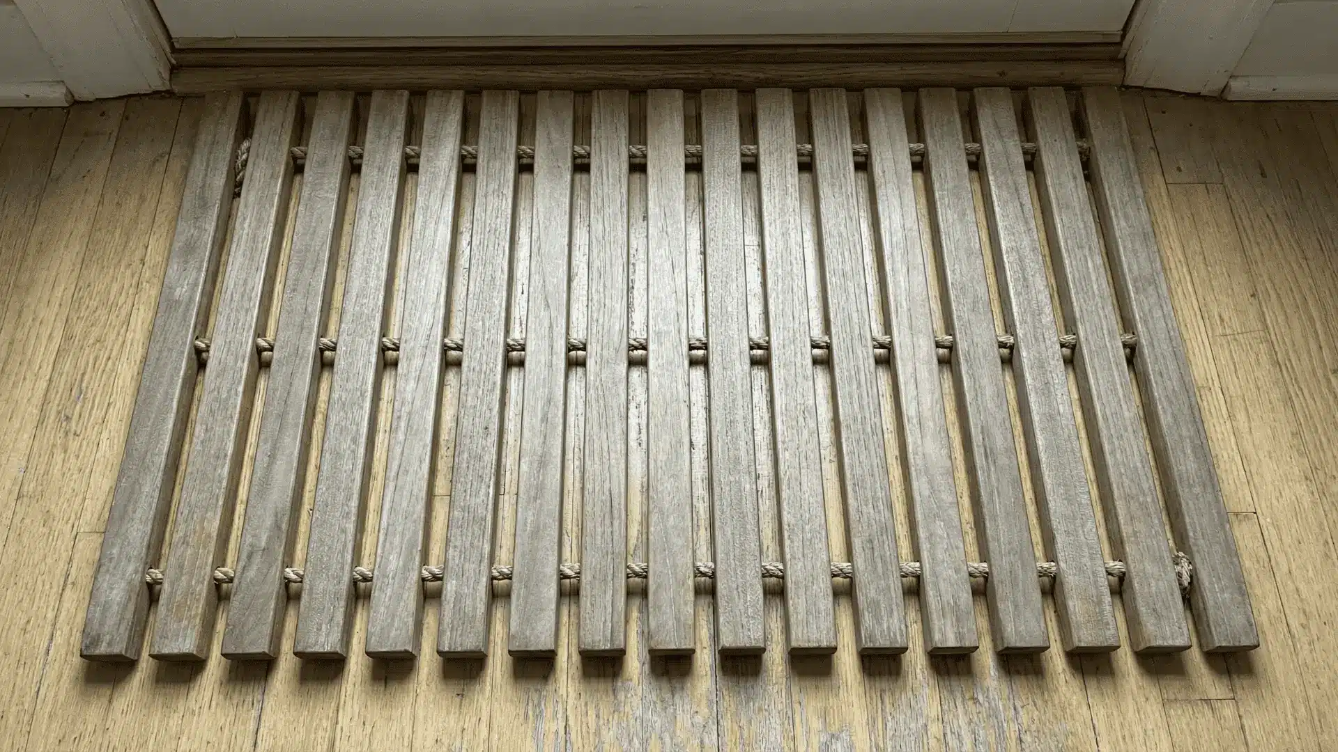 Wooden doormat with evenly spaced slats connected by rope placed on a floor