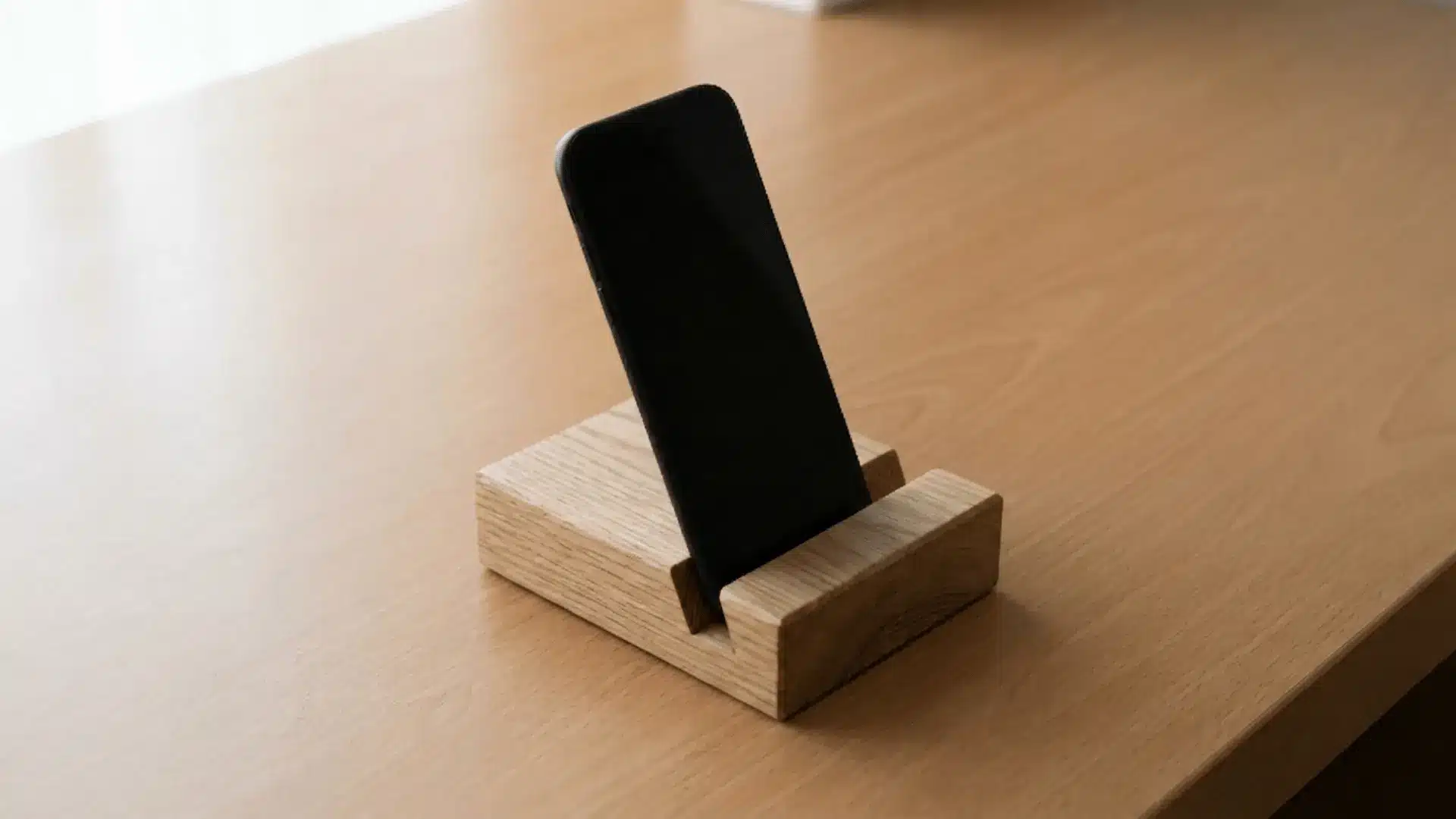 Wooden phone stand holding a smartphone at an angle on a flat desk surface