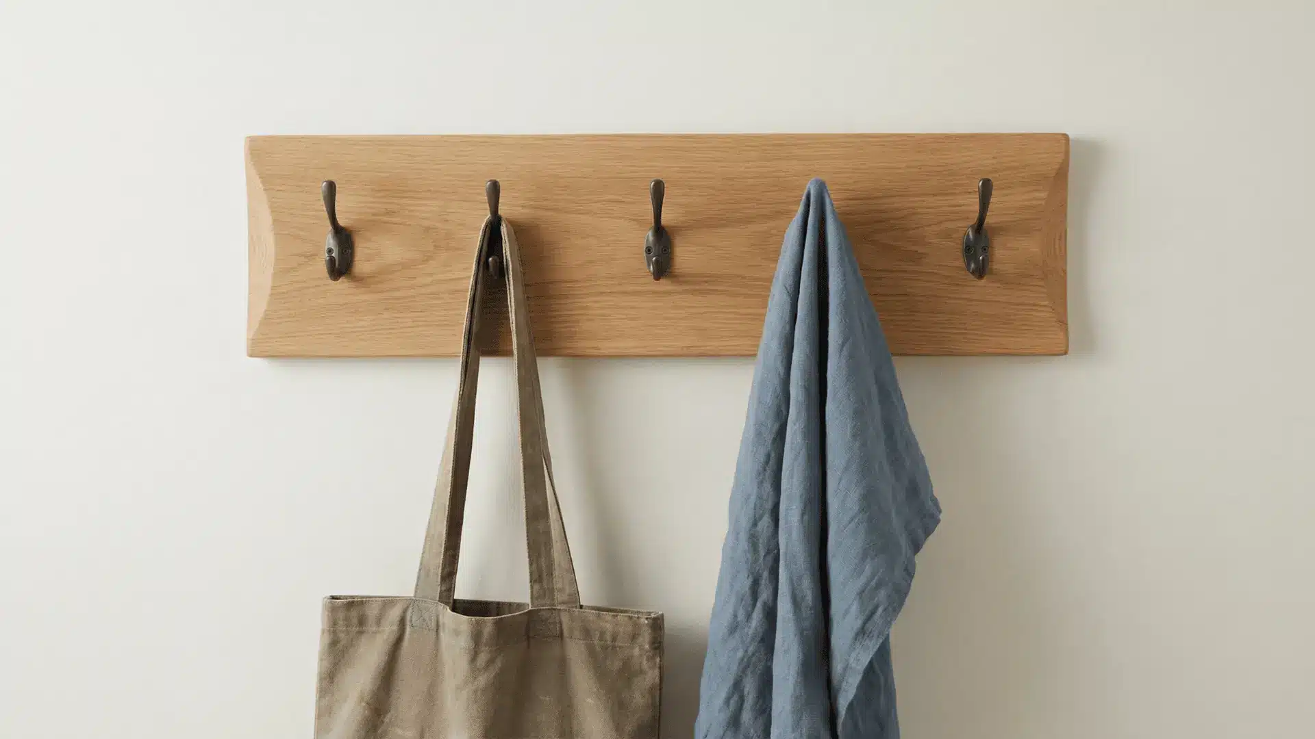 Wooden wall hooks board with evenly spaced hooks mounted on a wall holding a few items