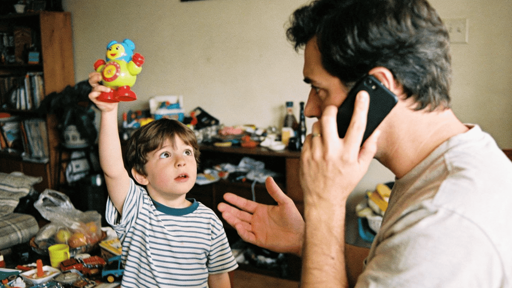 young boy showing toy to distracted father talking on phone in messy living room