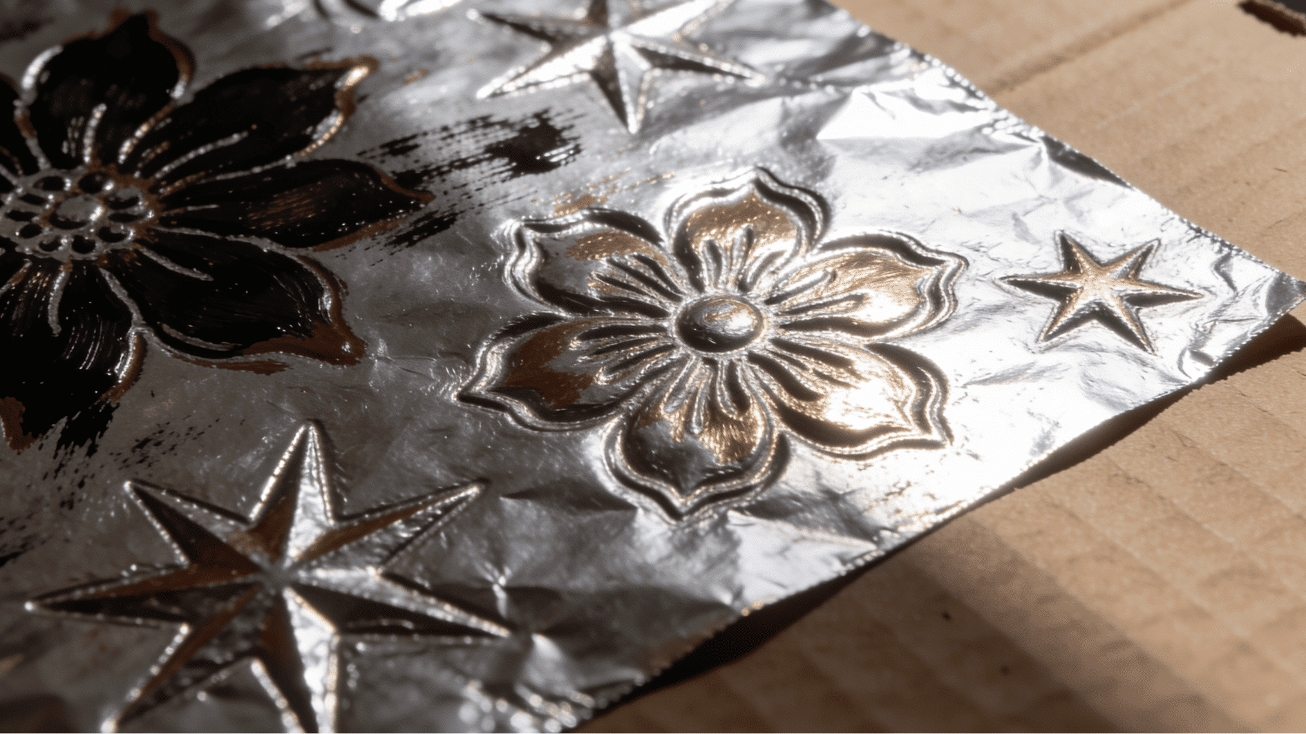 aluminium foil embossed art showing raised flower and star patterns with paint wiped back on cardboard