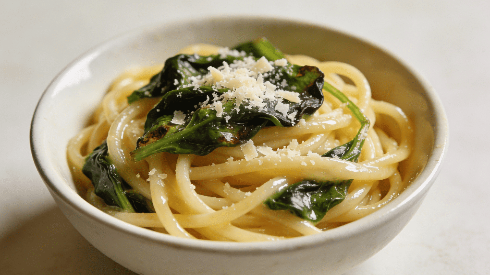 buttery spaghetti noodles with wilted spinach and parmesan in a white ceramic bowl