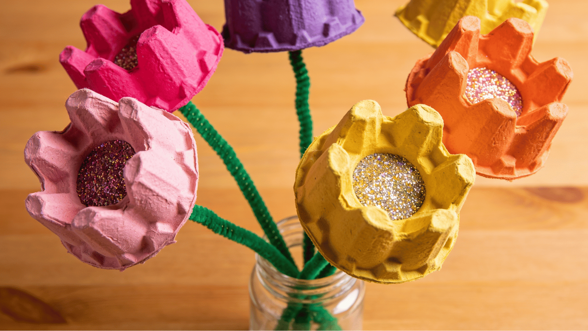 colorful egg carton flowers with glitter centers on pipe cleaner stems arranged in a glass jar