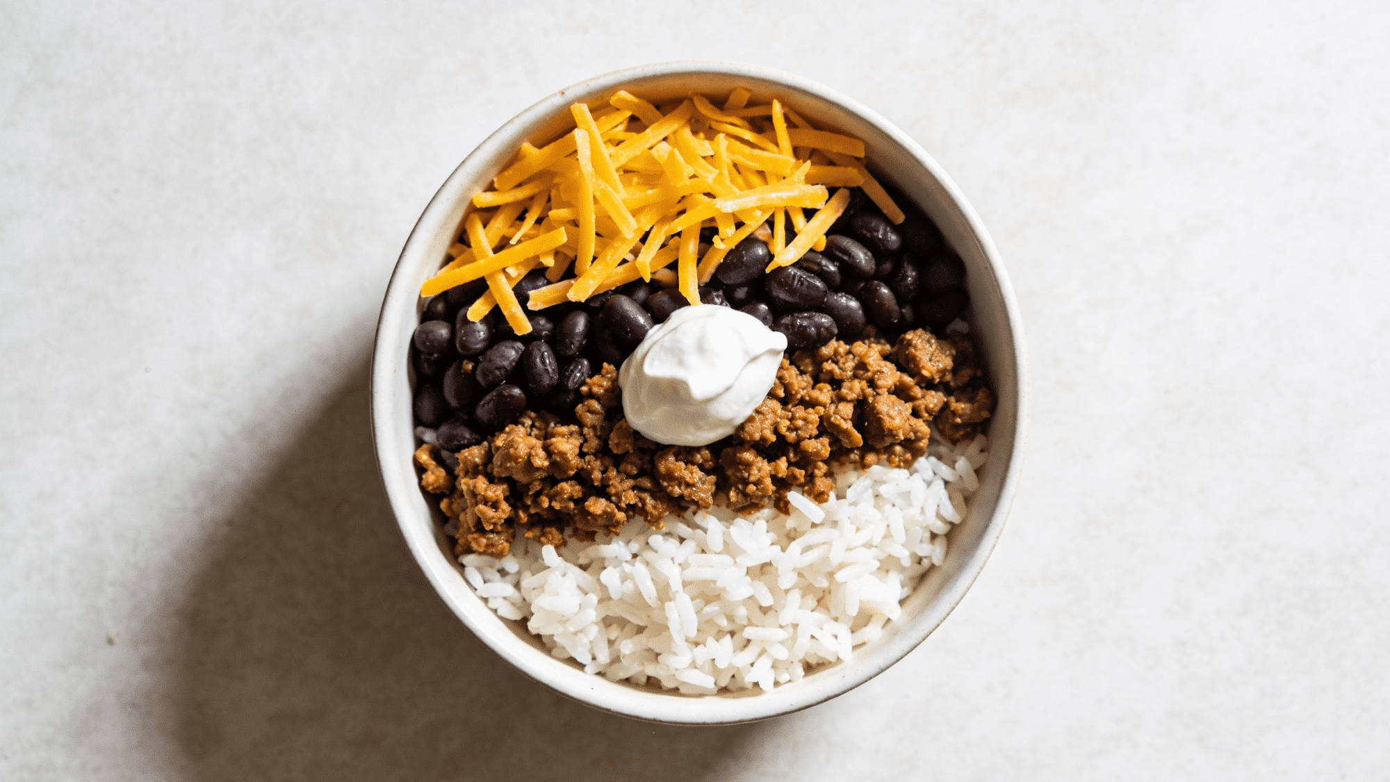 deconstructed taco bowl with rice, ground beef, black beans, cheddar, and sour cream