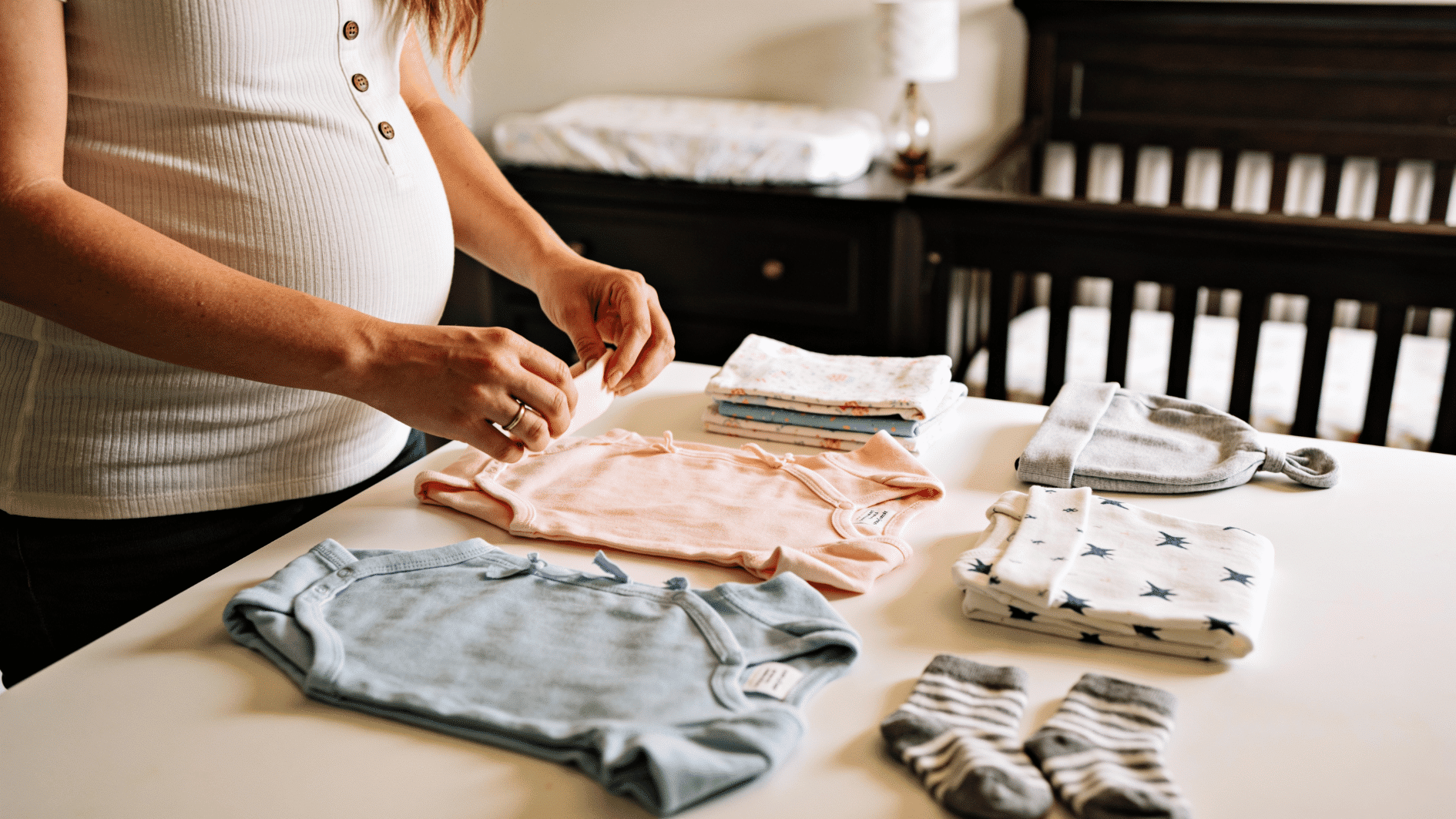 expectant parent organizing newborn clothes and essentials on a table in a nursery while preparing for baby arrival