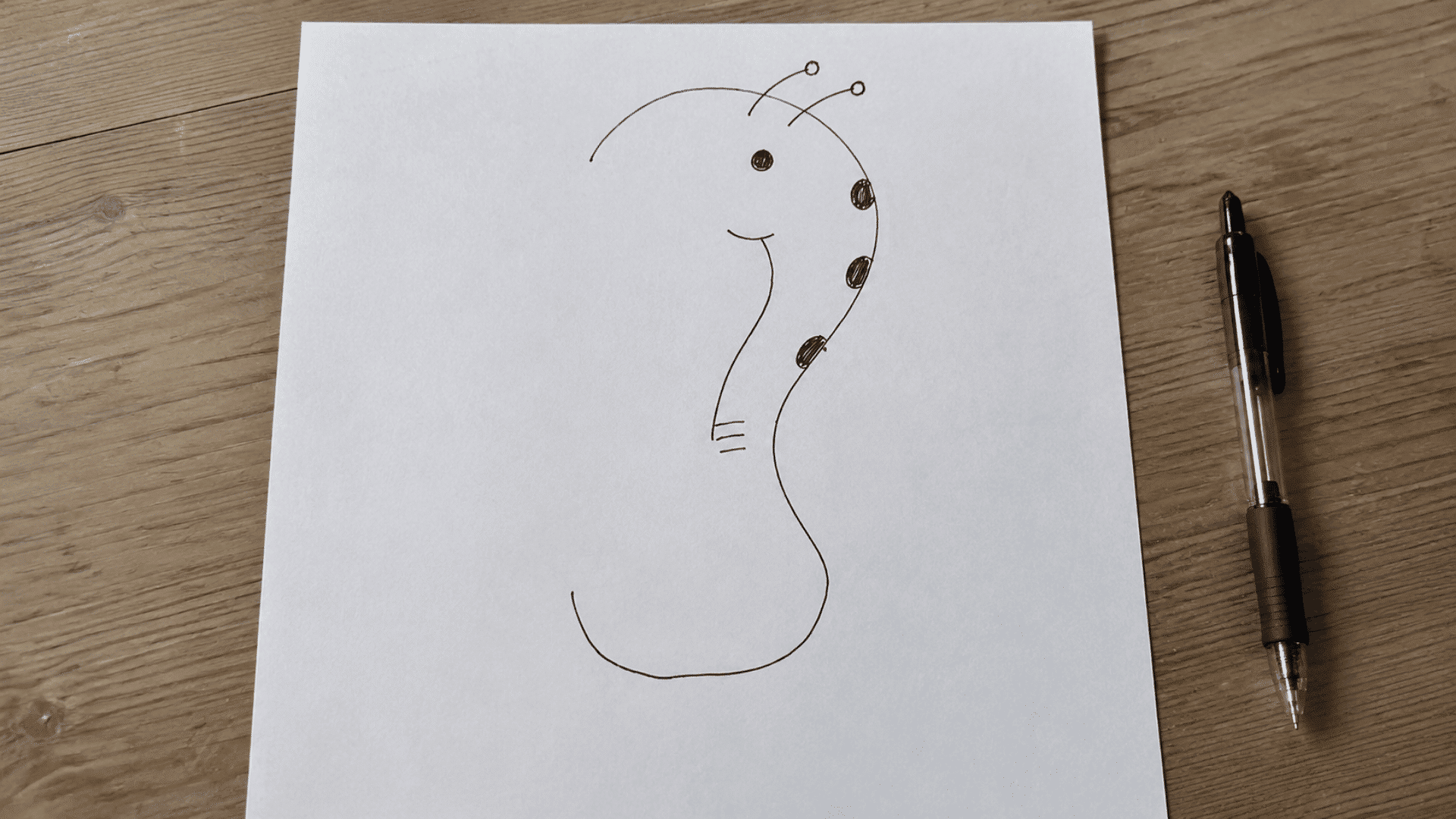 finish the drawing pen and paper games setup with white paper half finished drawing and a pen on side on a wooden desk