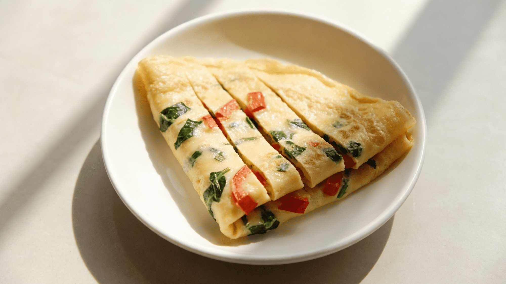 folded soft yellow omelet with red bell pepper and spinach sliced into strips on a plate