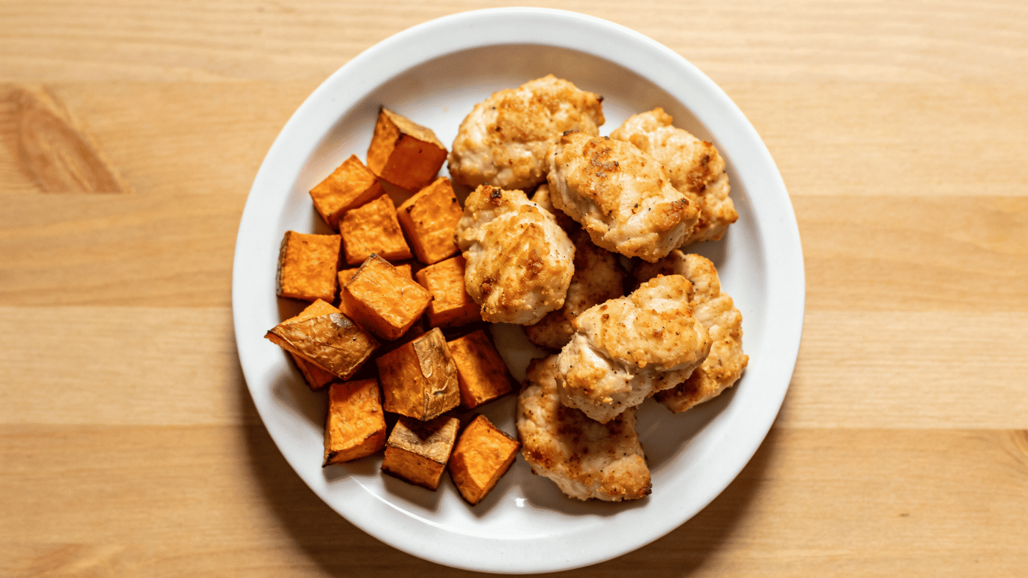 homemade baked chicken nuggets and golden roasted sweet potato cubes on a baking tray