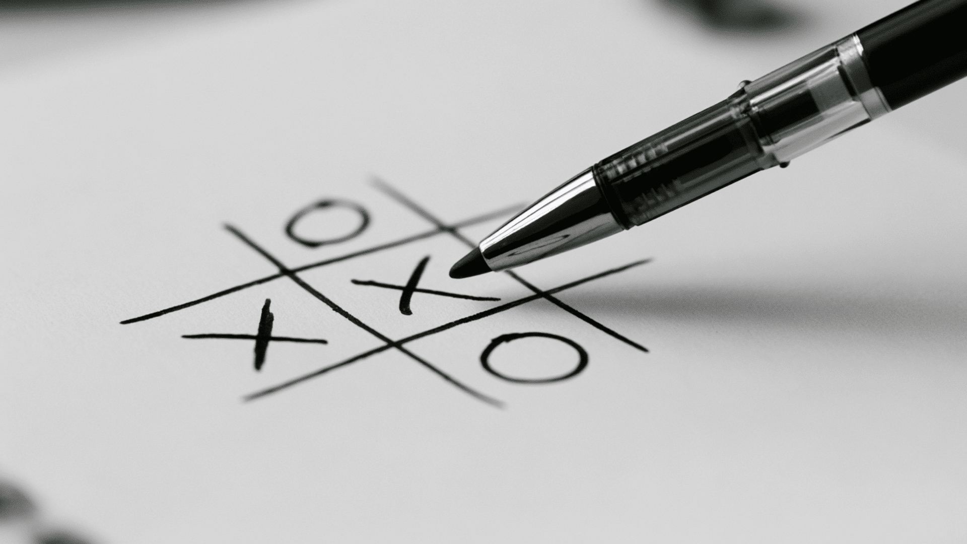 image of pen and paper game tic tac toe using a black sketch pen on a white paper with visible x and o letters