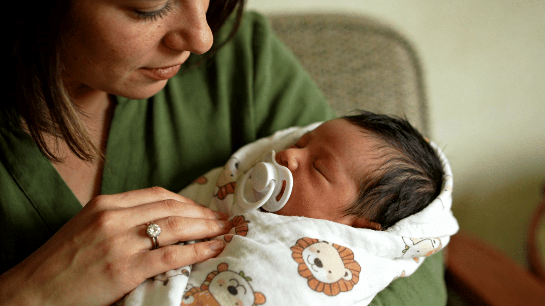 mother holding sleeping newborn wrapped in animal blanket with pacifier during calm bonding moment indoors
