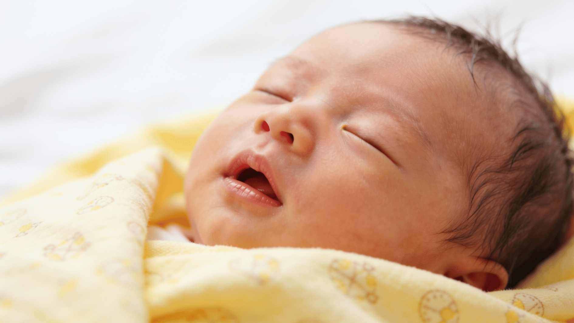 newborn baby sleeping under a yellow blanket with relaxed features and soft natural lighting creating a calm scene