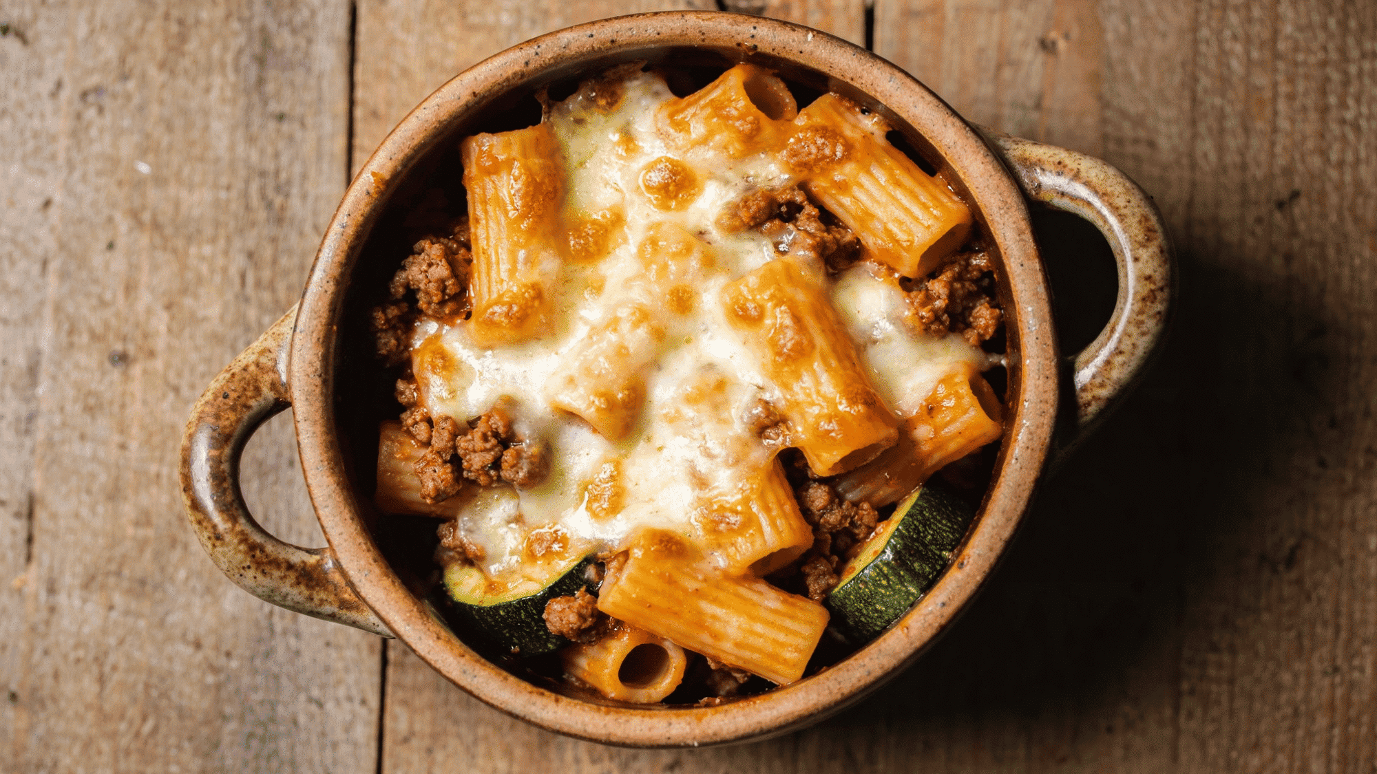 pasta bake with bubbly golden mozzarella crust, zucchini, and ground beef in a baking dish